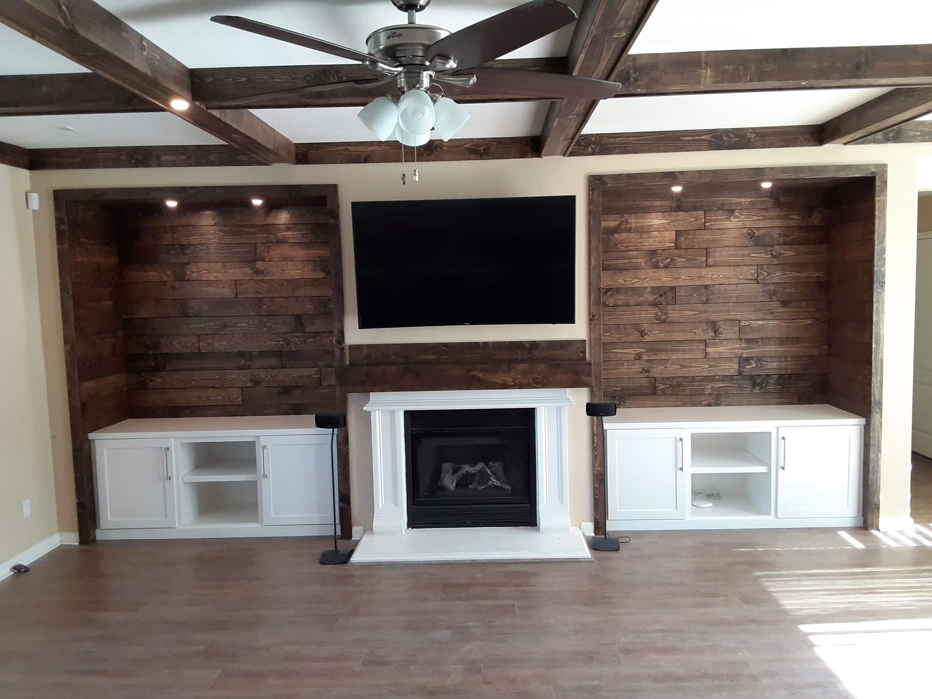 Living room with a wall-mounted TV, white fireplace, built-in cabinets, wood beams, and hardwood floor