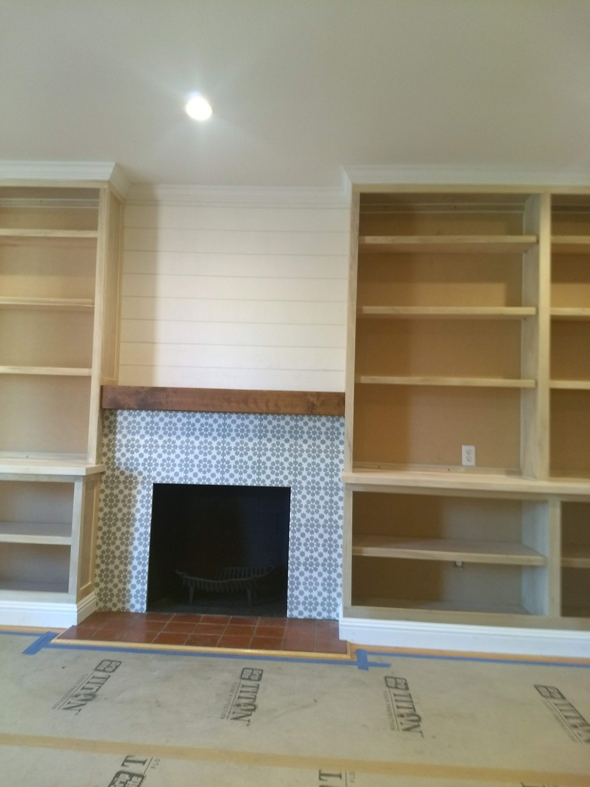 Built-in fireplace flanked by empty wooden shelves in a carpeted room under construction