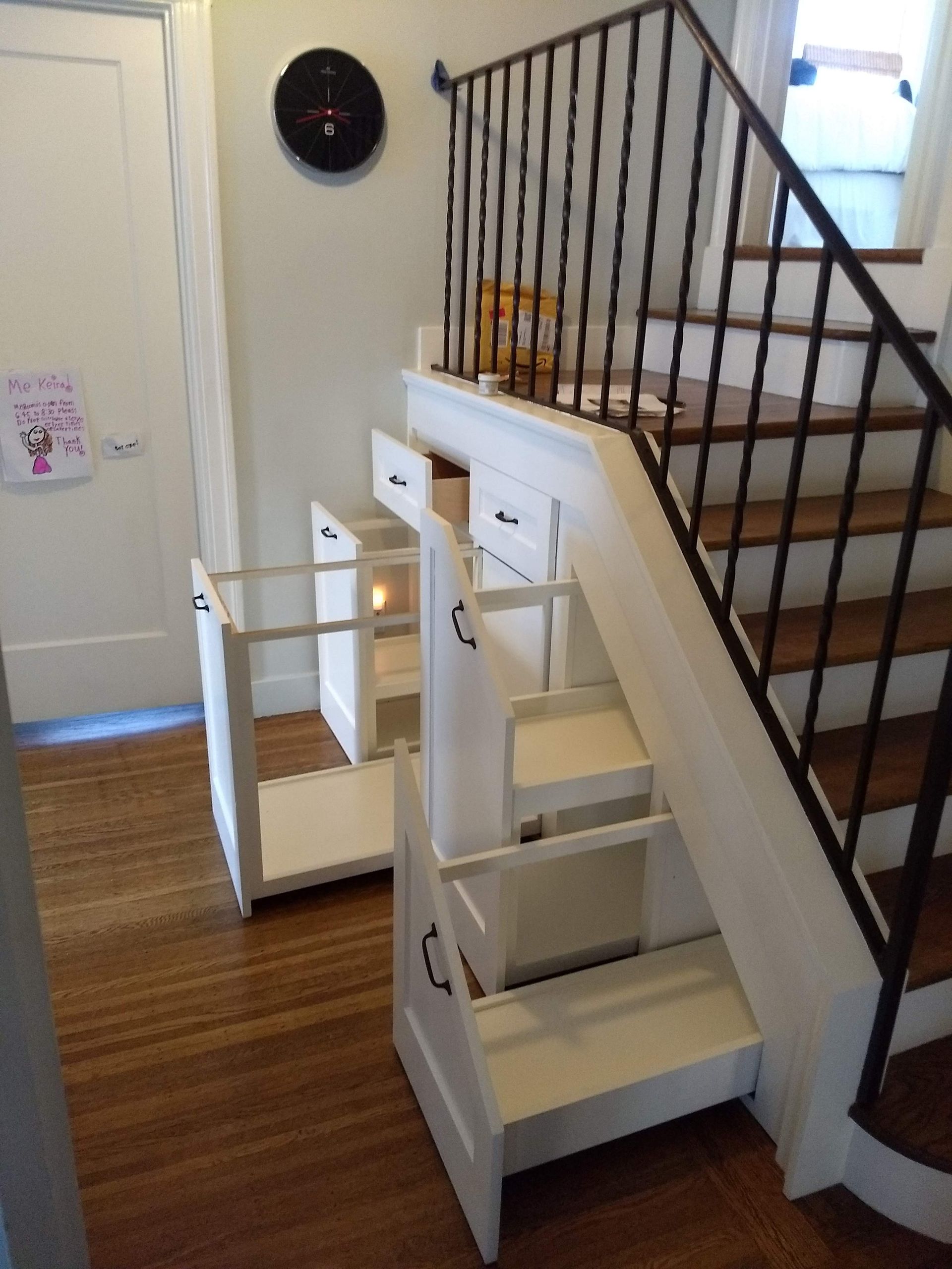 White stairlift beside a staircase in a home interior, with a wooden floor and white walls.