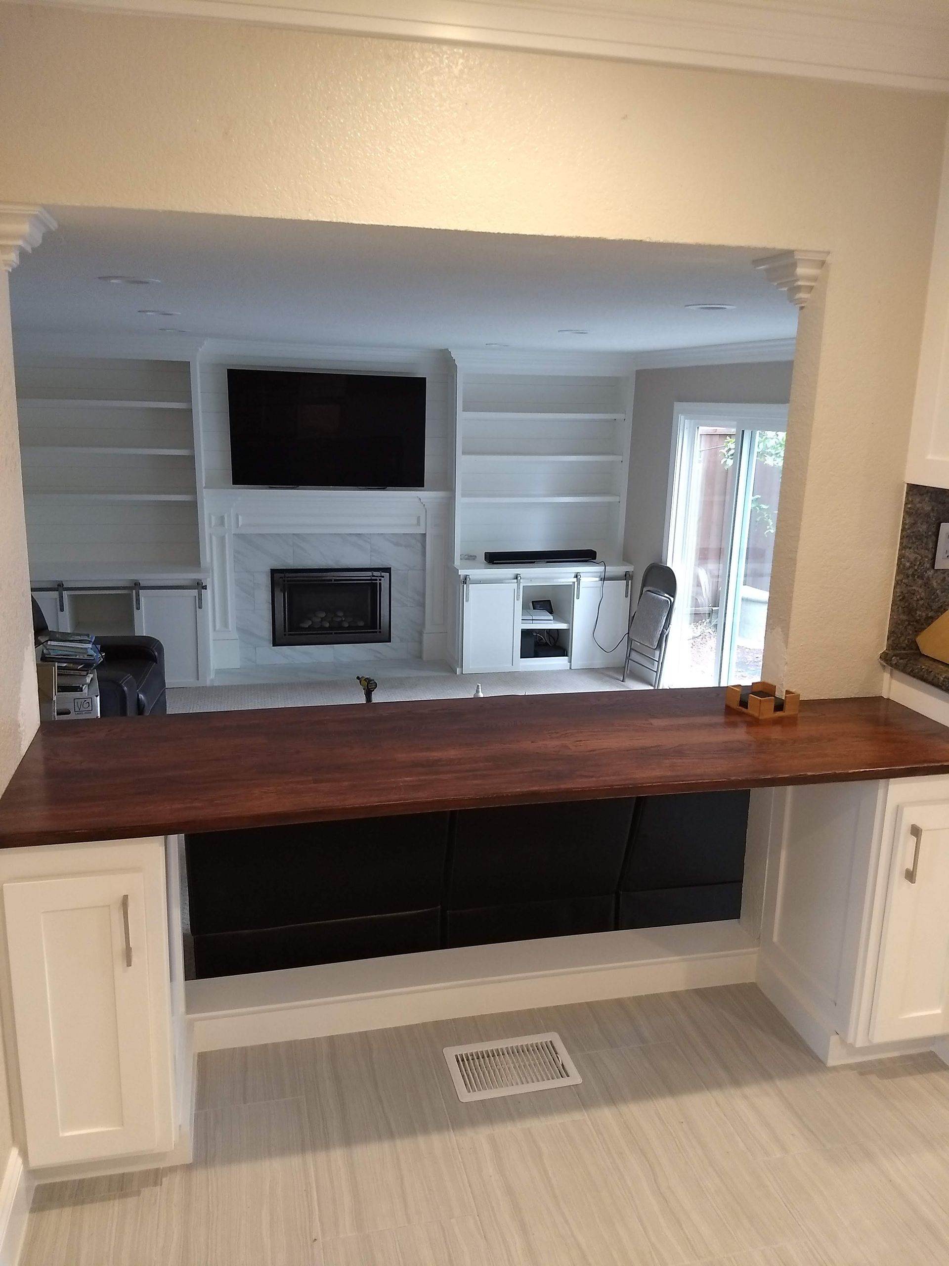 Kitchen pass-through with dark wood counter, white cabinets, and a fireplace visible through the opening