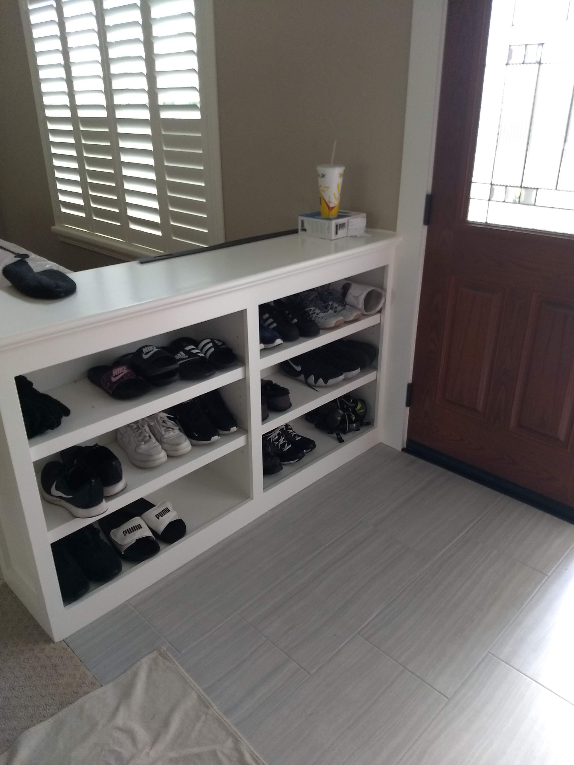 White entryway cubby with shoes, a mirror, a front door, and light gray flooring
