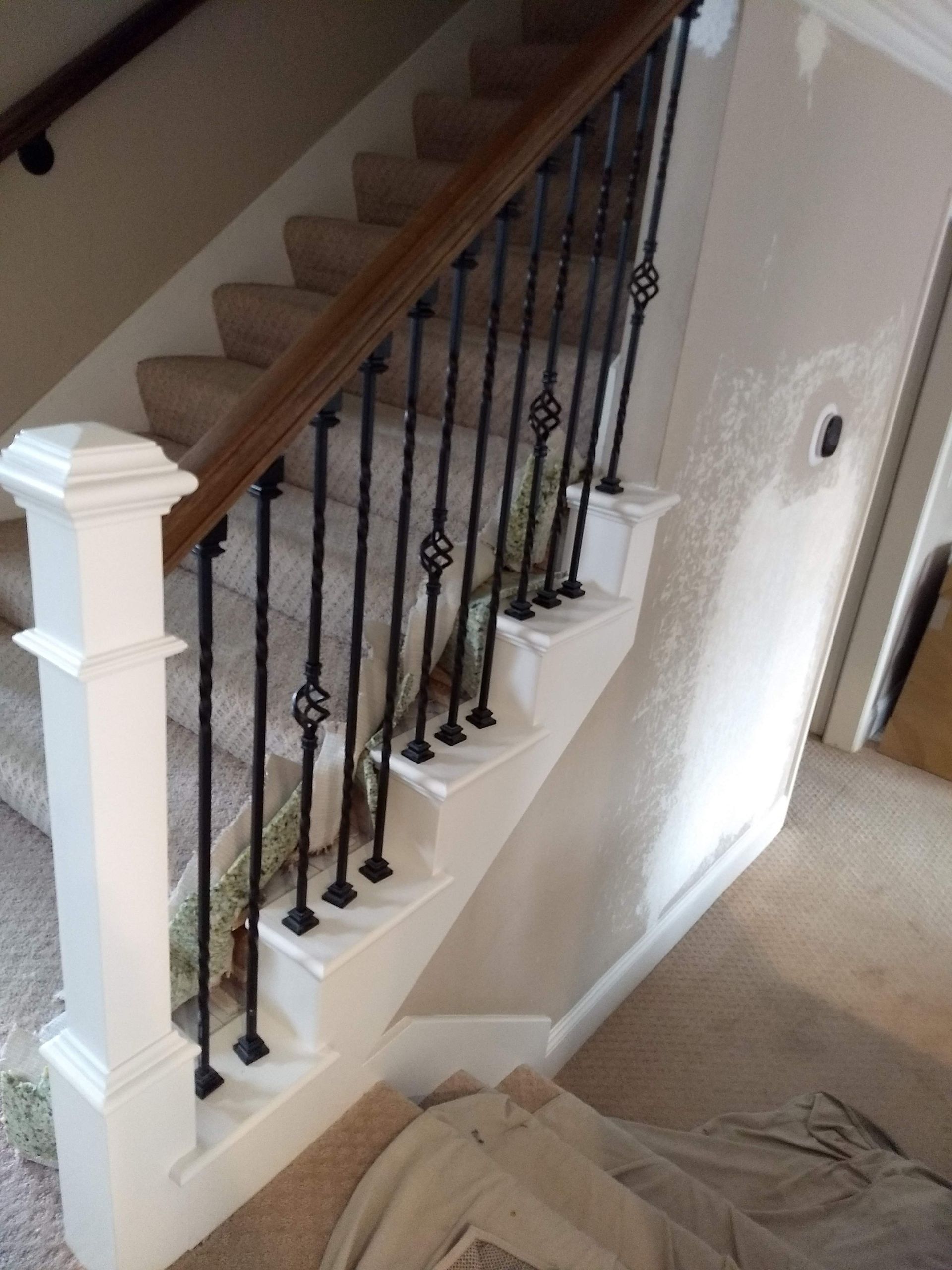 Staircase with white railing, dark iron balusters, and beige carpet in a home interior