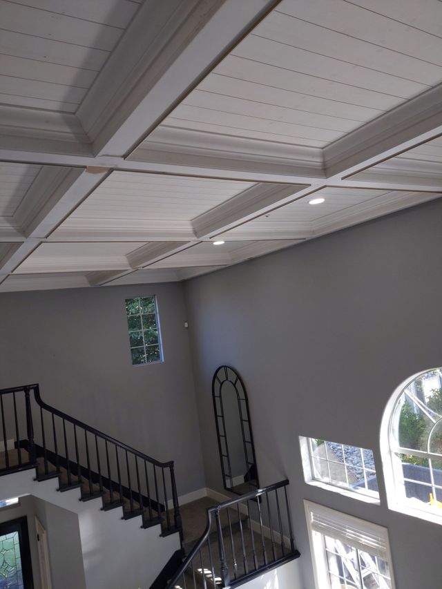 Interior stairwell with black railing, white ceiling beams, and arched windows letting in daylight