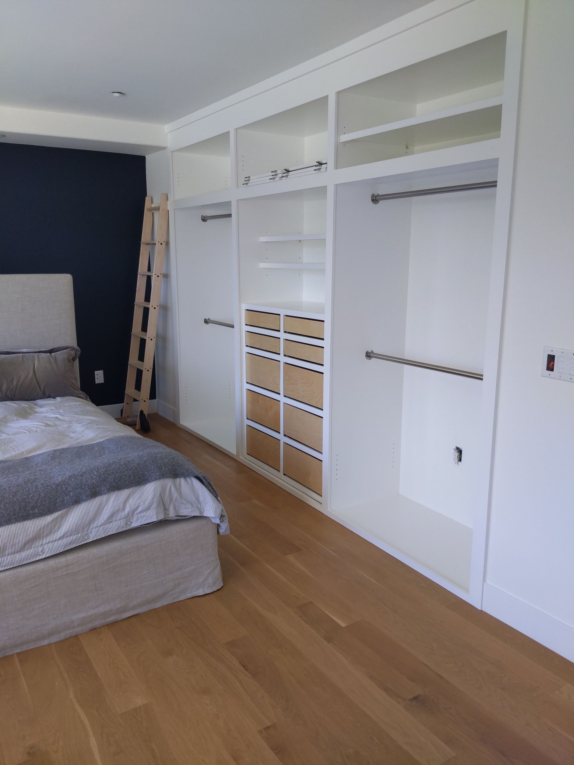 Bedroom with bed, ladder, and built-in white closets over wood flooring.