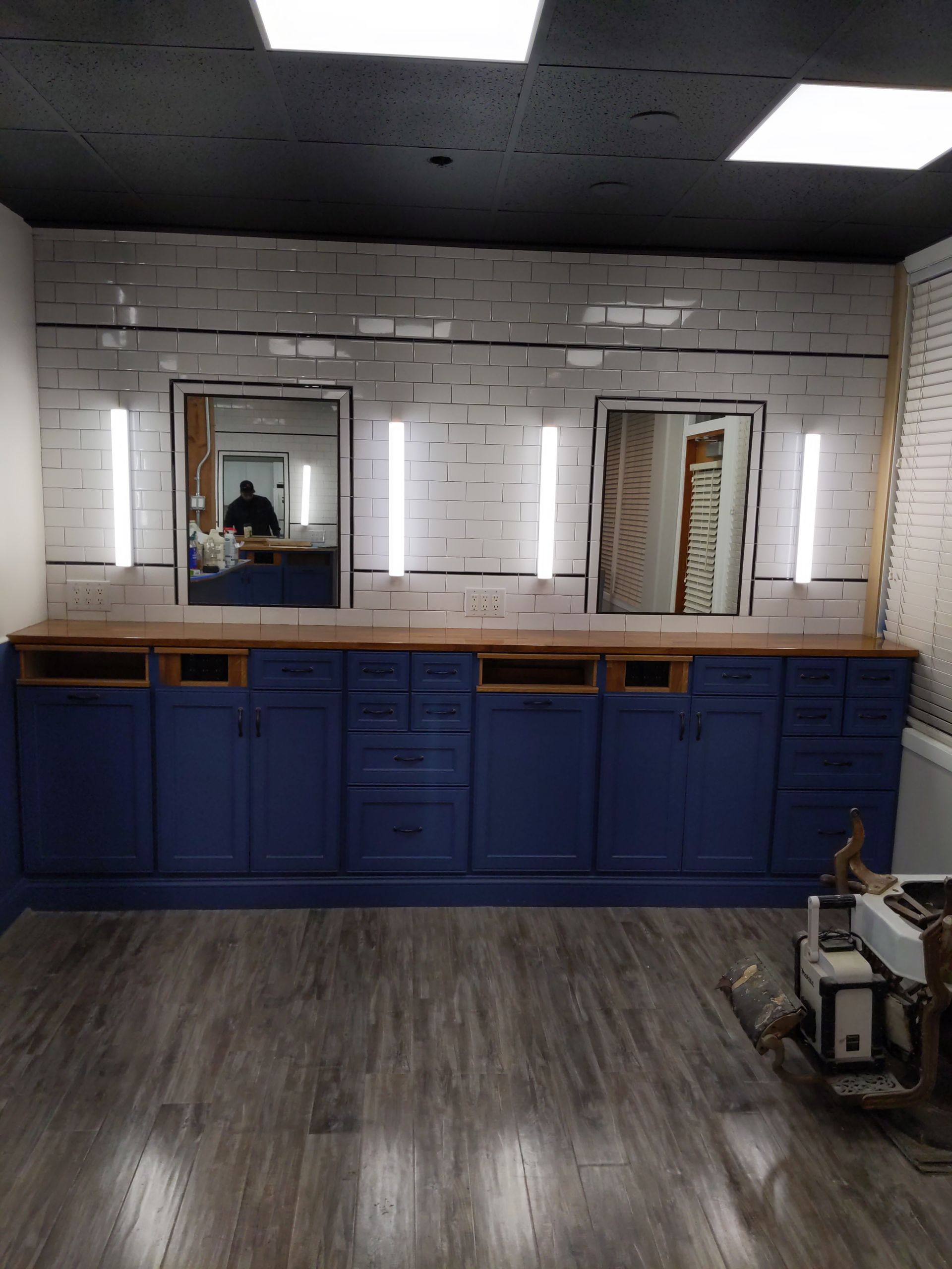 Modern bathroom with blue vanity, large mirrors, and gray tile floor under fluorescent lights
