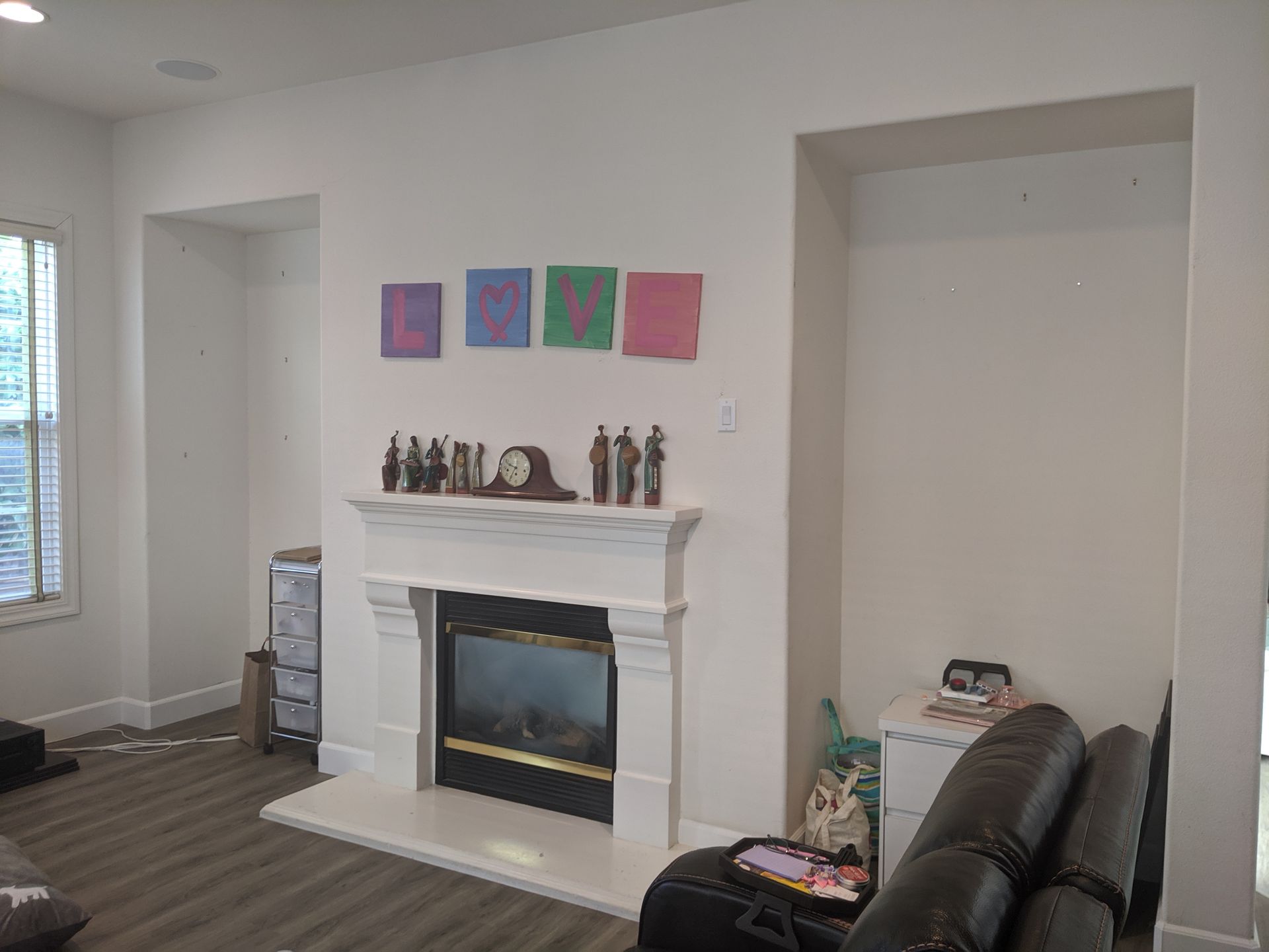 Living room with white fireplace, wall art, and a black chair beside a large empty alcove.