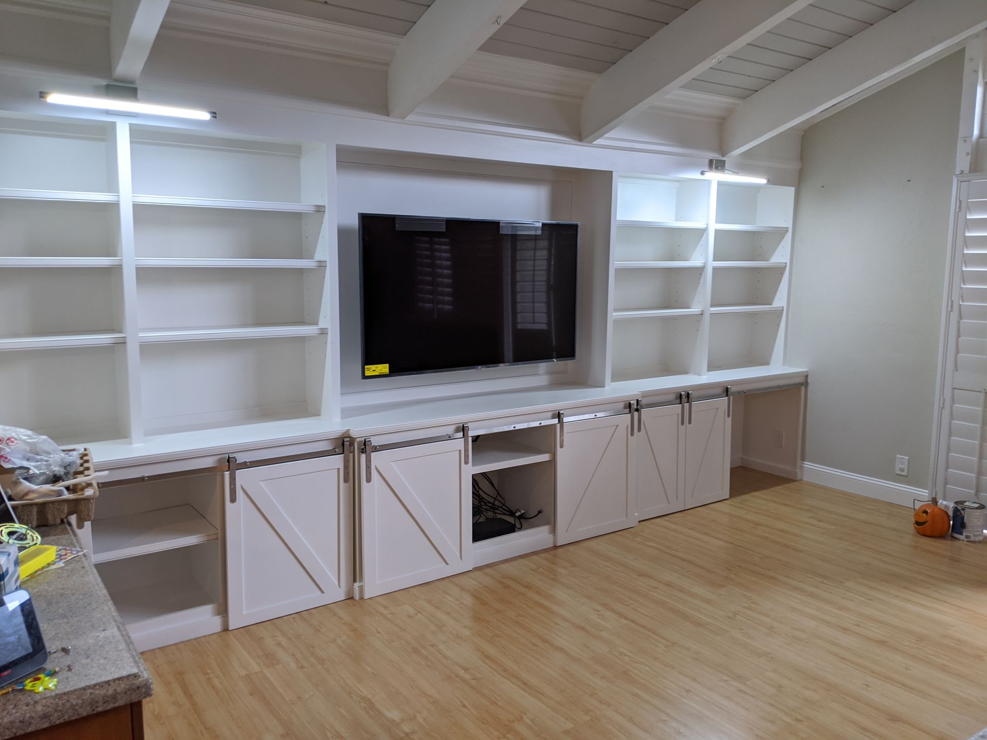 Bright room with built-in white shelves, cabinets, and a wall-mounted TV above hardwood flooring.