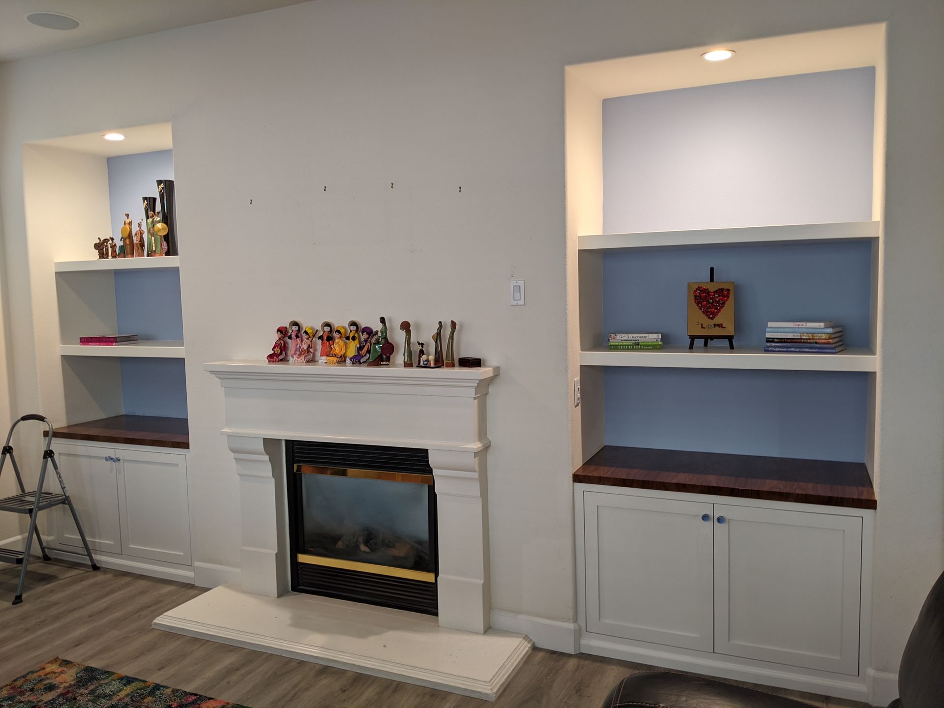 Living room with white built-in shelves and cabinets flanking a fireplace, holding decor and trophies.