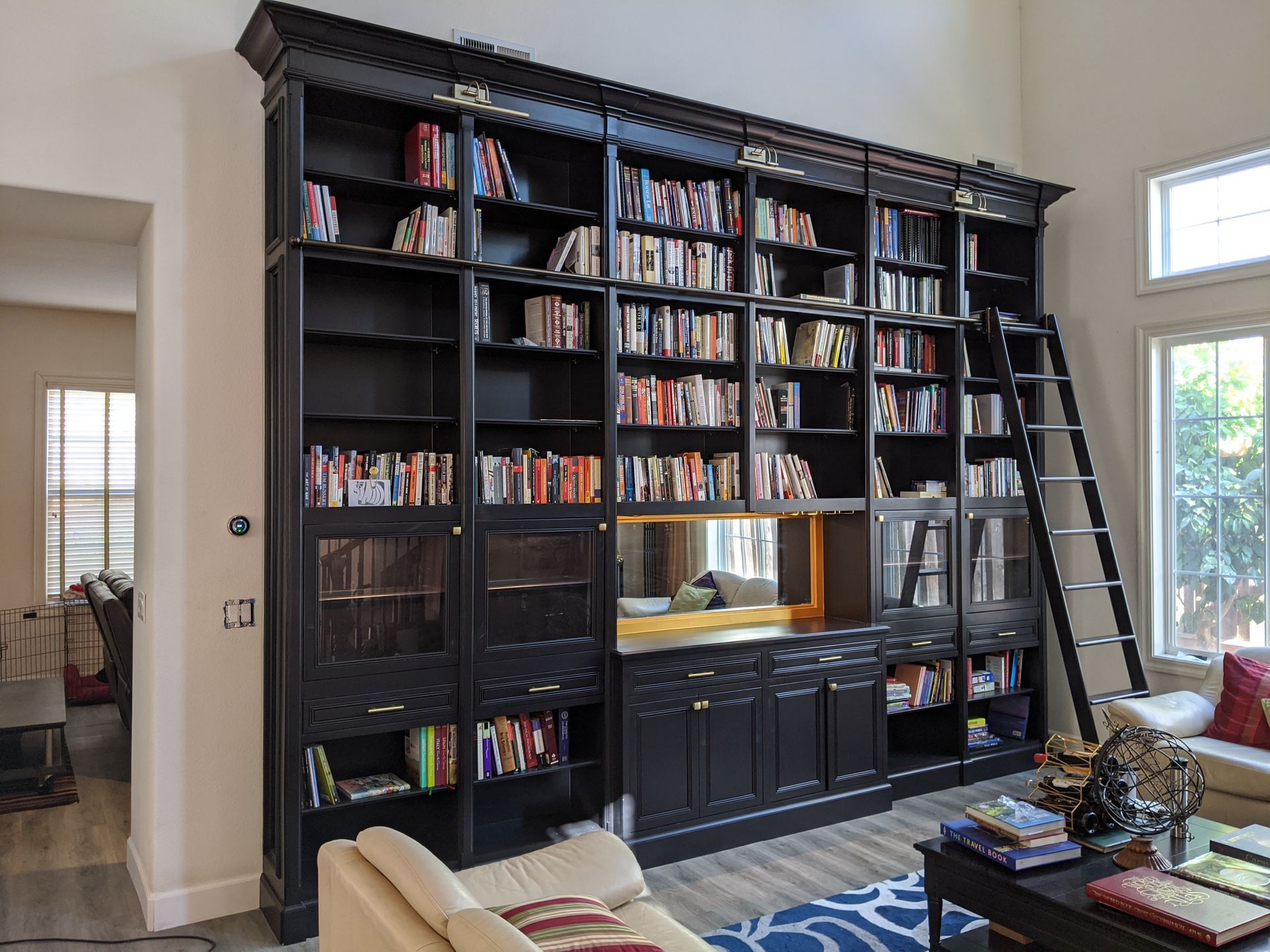 Tall black bookshelf filled with books in a bright living room beside a doorway and window
