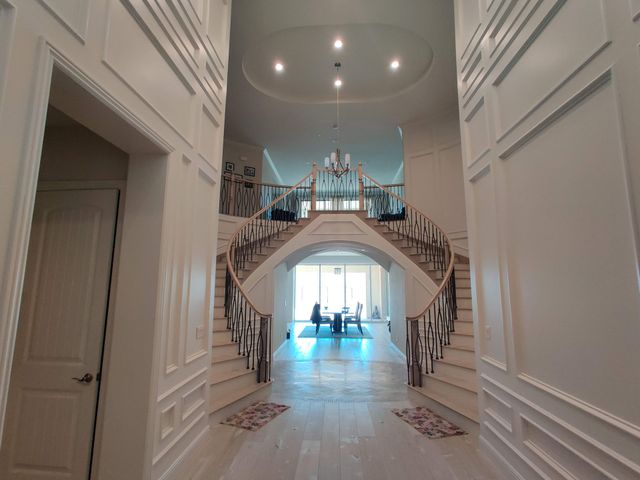 Grand foyer with a sweeping staircase, chandelier, and bright doorway at the far end