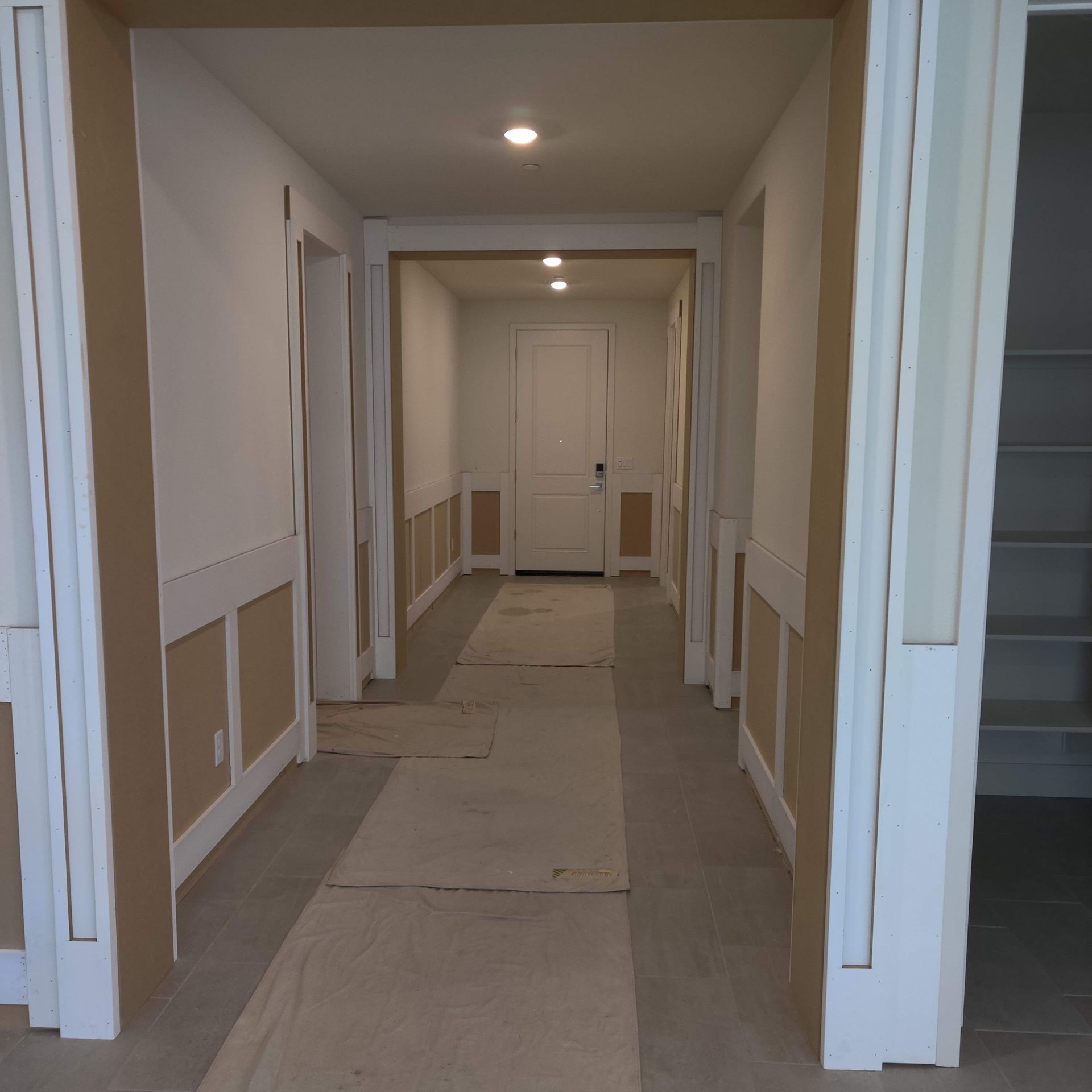 Renovated white hallway with covered floor, recessed lights, and doorways leading to a back door.