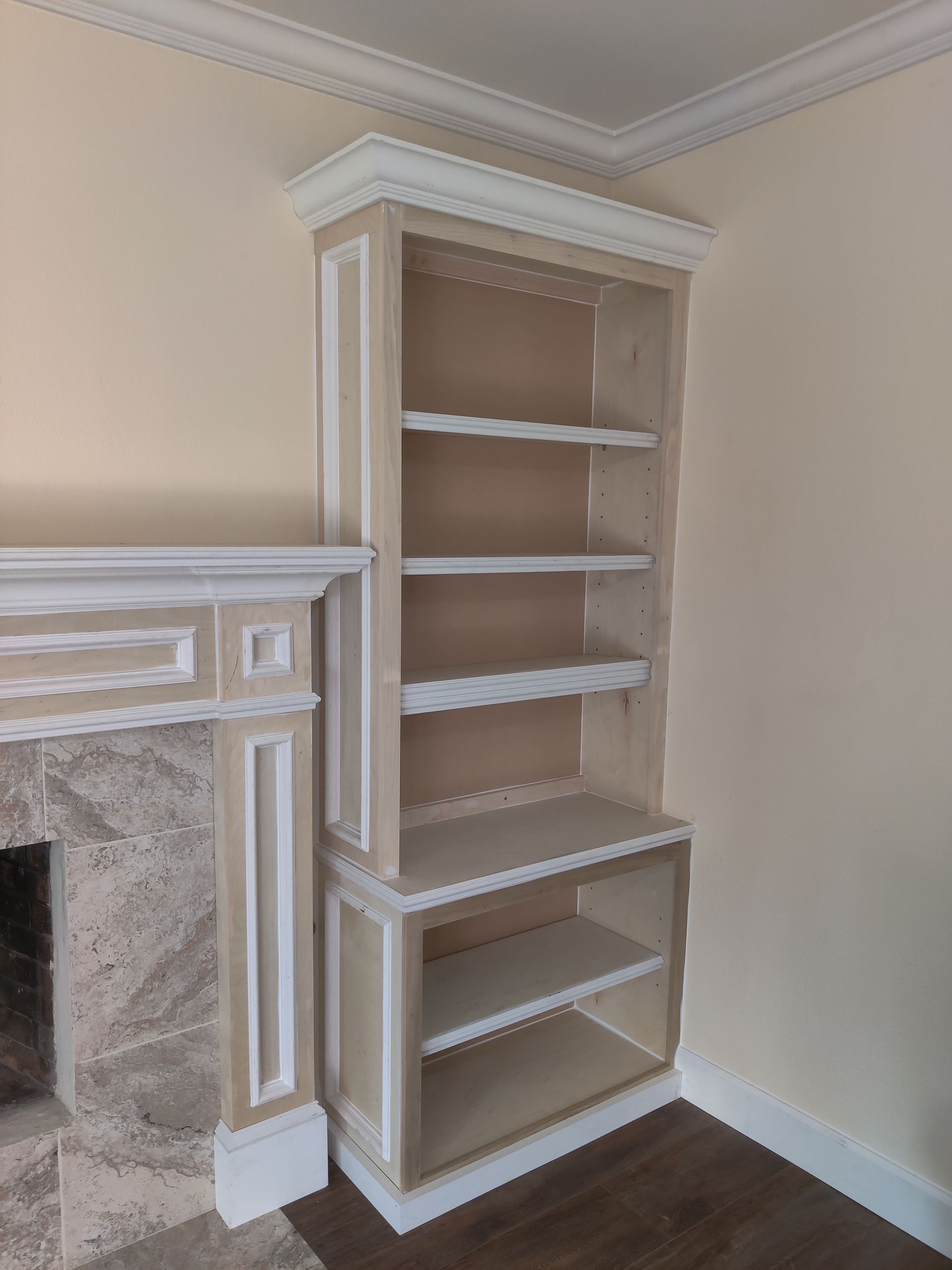 Built-in beige bookshelf beside a white fireplace in an empty room