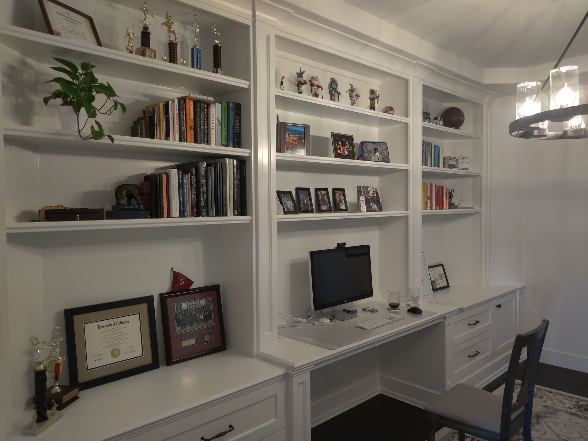 Built-in white office shelves and desk with books, framed photos, and a computer monitor.