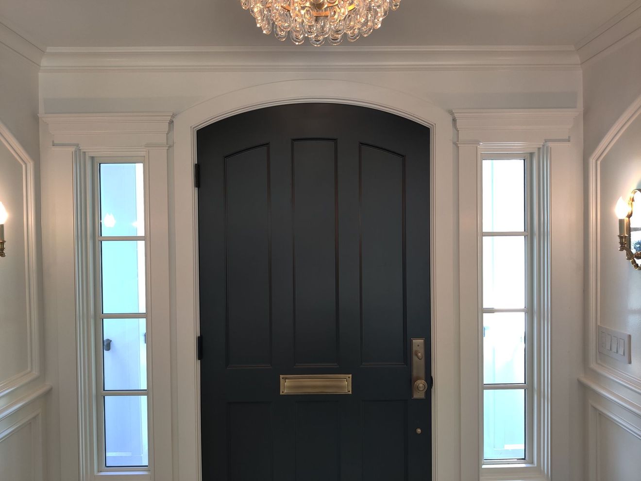 Front entry with a black double door, sidelights, white paneled walls, and a chandelier overhead