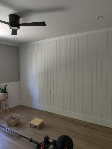 Bright room with white paneled walls, wood floor, ceiling fan, and scattered exercise items on the floor
