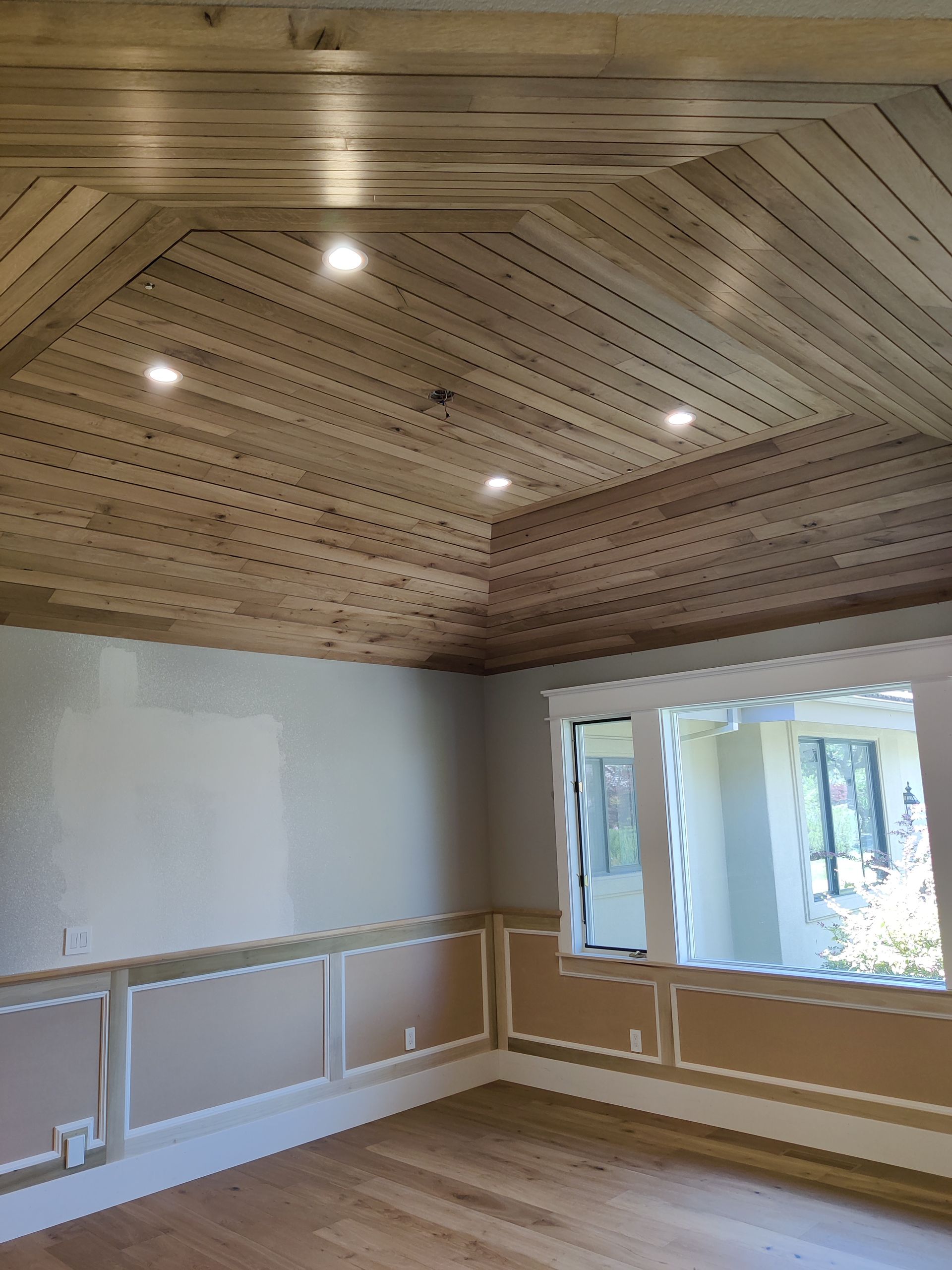 Empty room with a wood-paneled vaulted ceiling, white walls, and large windows