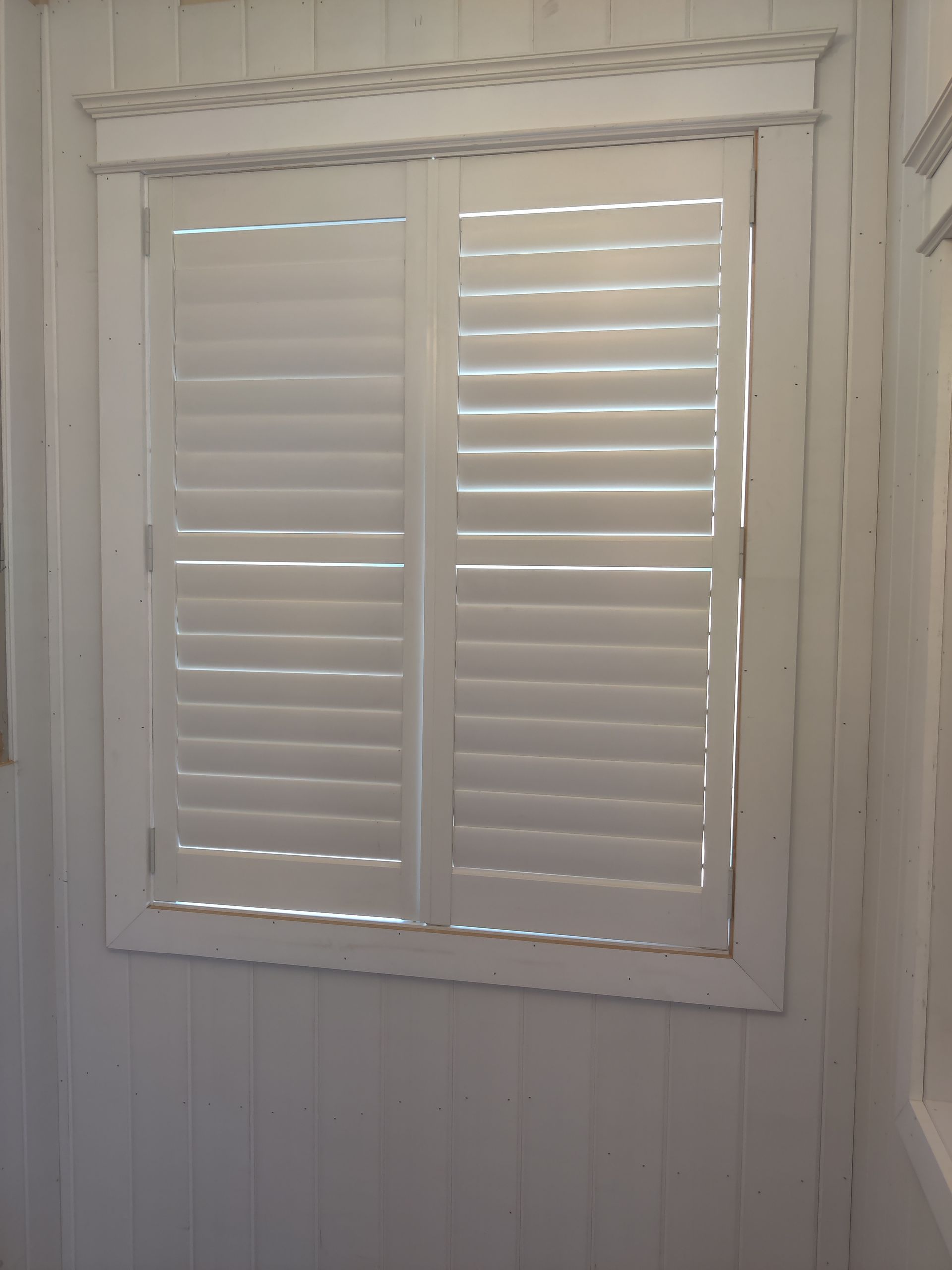 White plantation shutters on a small window in a white paneled wall