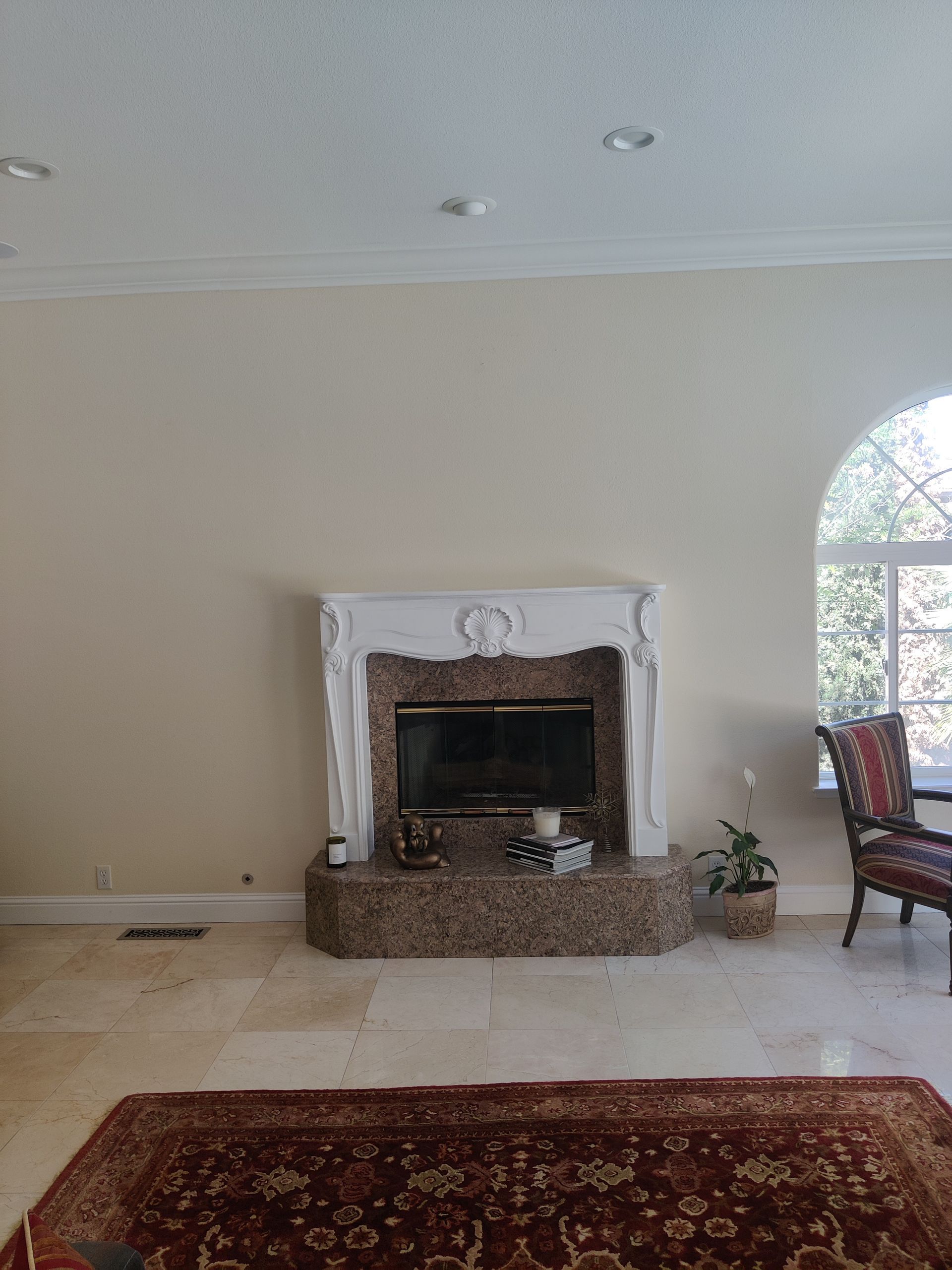Living room with white fireplace, beige walls, red rug, and arched window beside a chair and plant