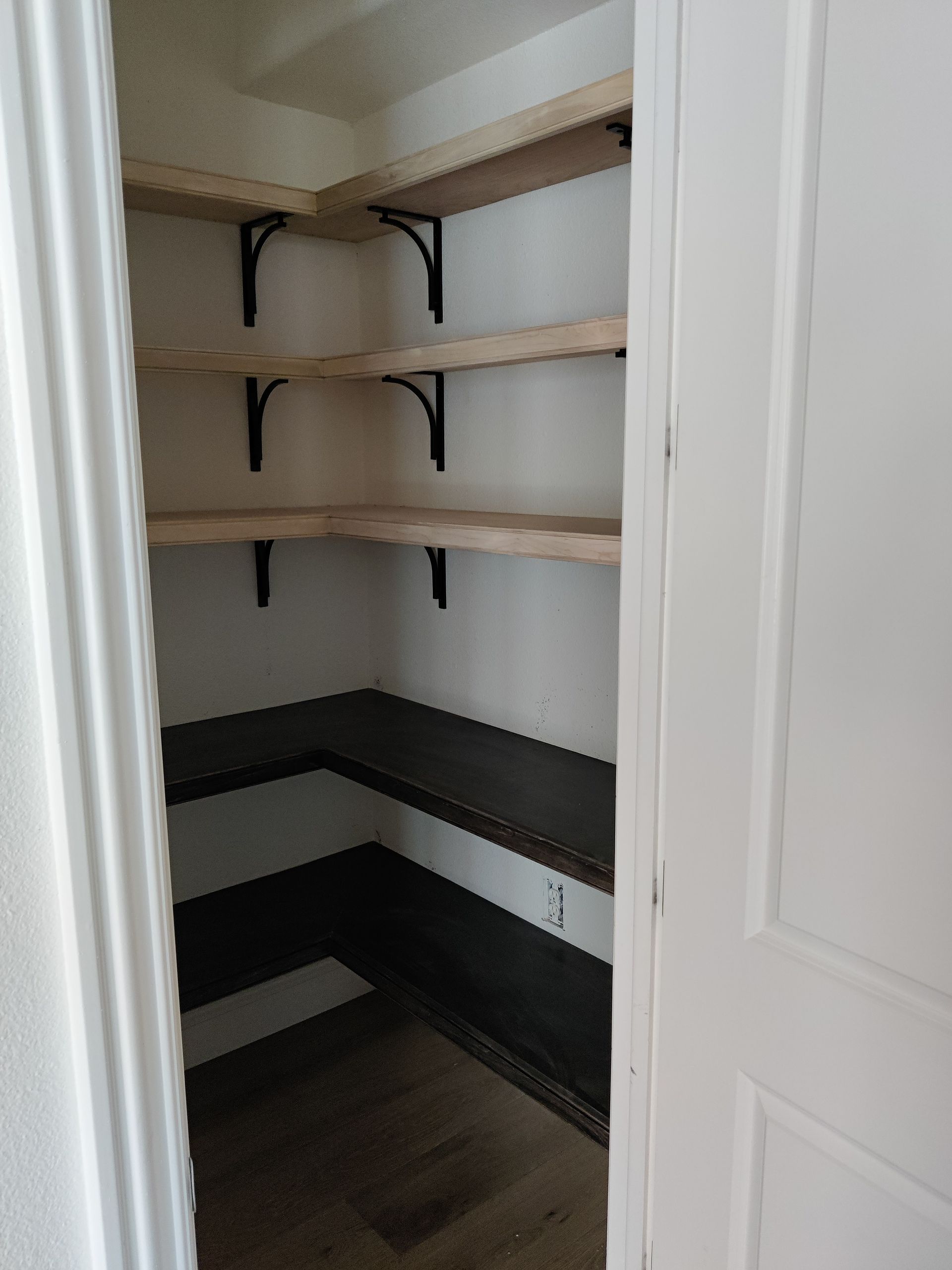 White closet pantry with wooden shelves and dark lower shelving, viewed through open doors
