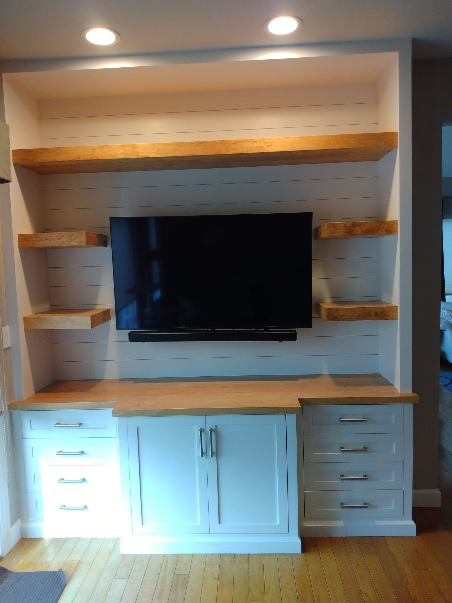 White built-in entertainment center with wood shelves and a TV in the middle.