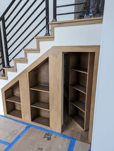 Built-in under-stair wooden storage shelves with open cubbies and blue tape on the floor