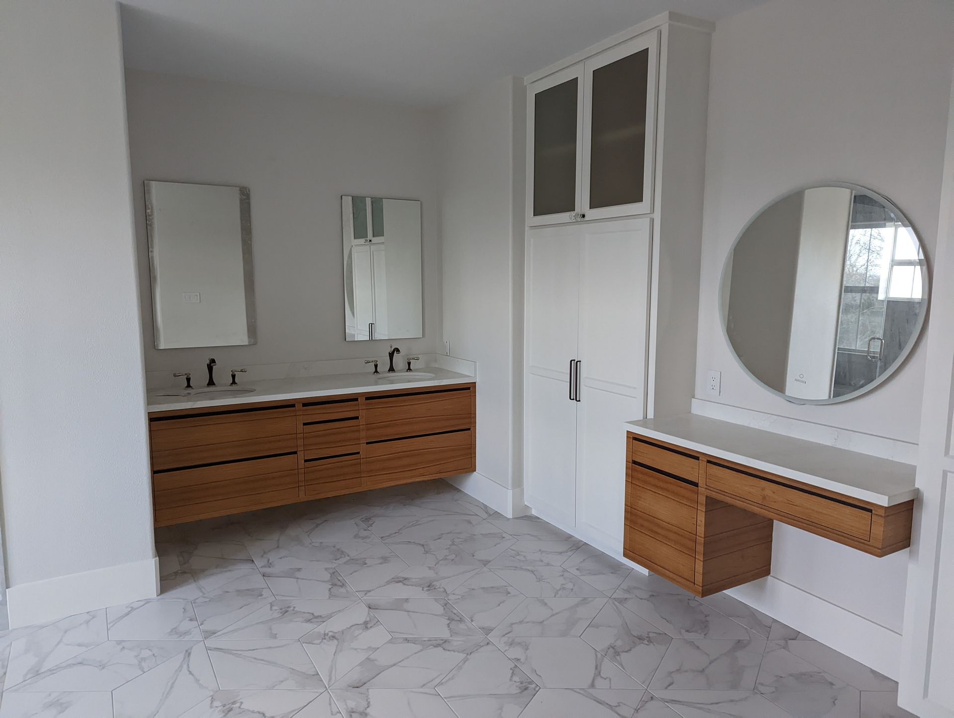 Bright bathroom with double vanity, mirrors, white walls, marble floor, and round wall mirror.