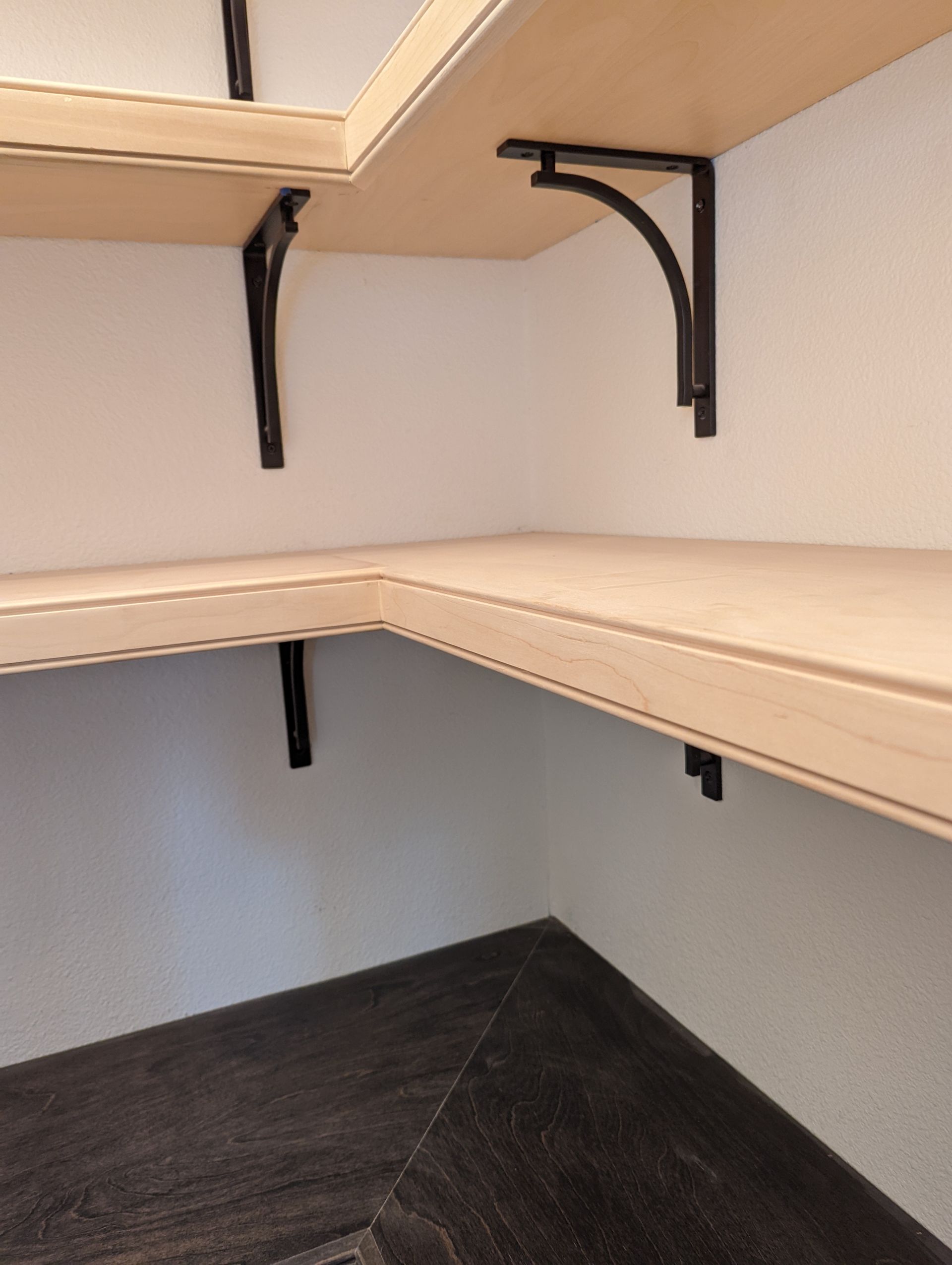 Empty closet shelves with beige wood and black metal brackets.