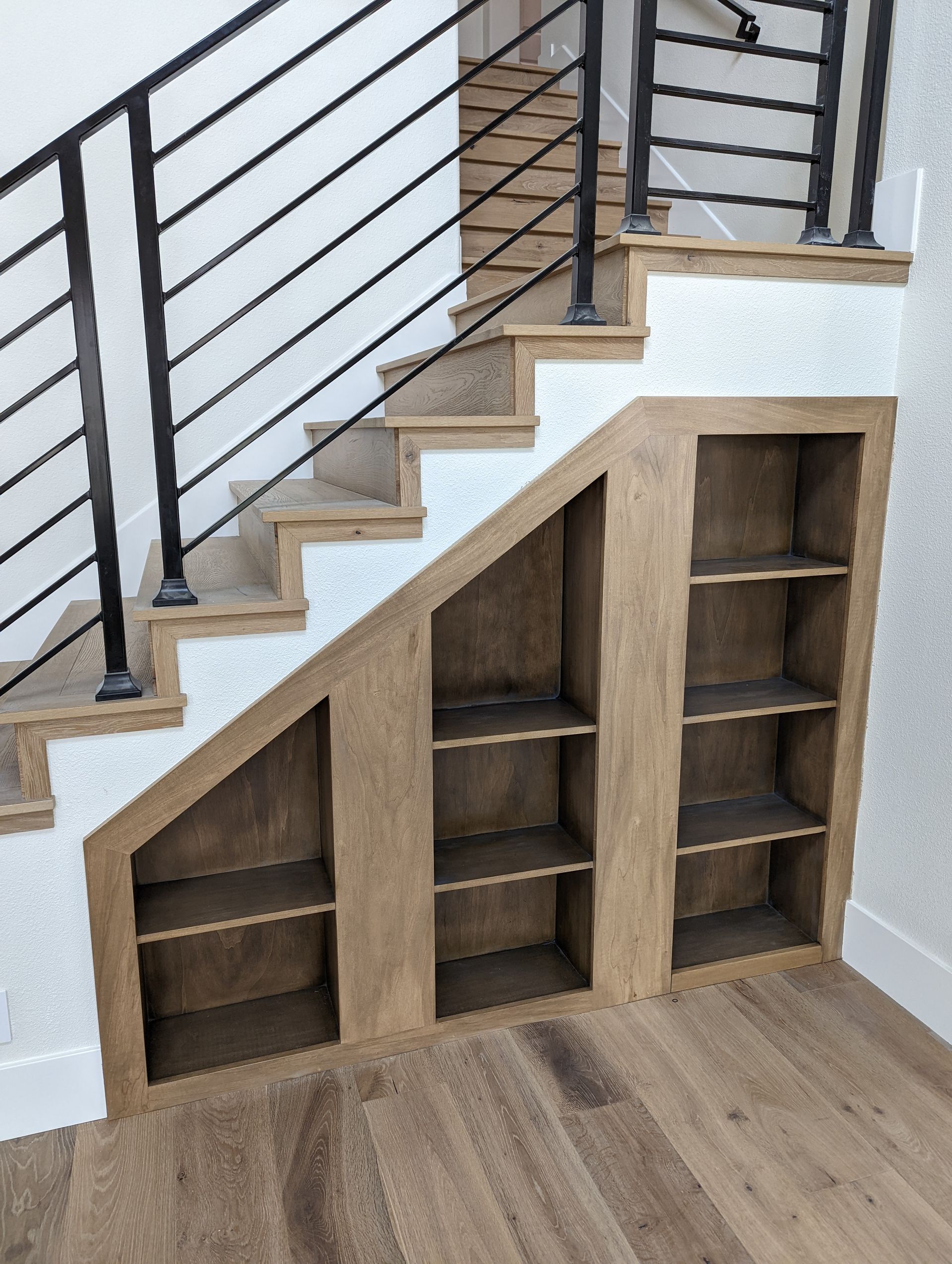 Built-in wooden storage under staircase with black metal railing and wood floor