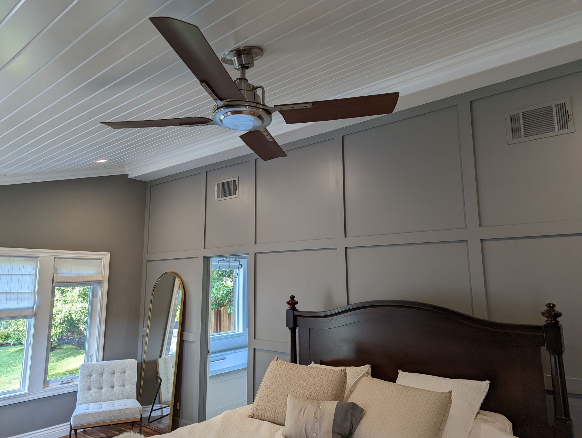 Bedroom with dark wood bed, mirrored dresser, ceiling fan, and gray paneled walls.