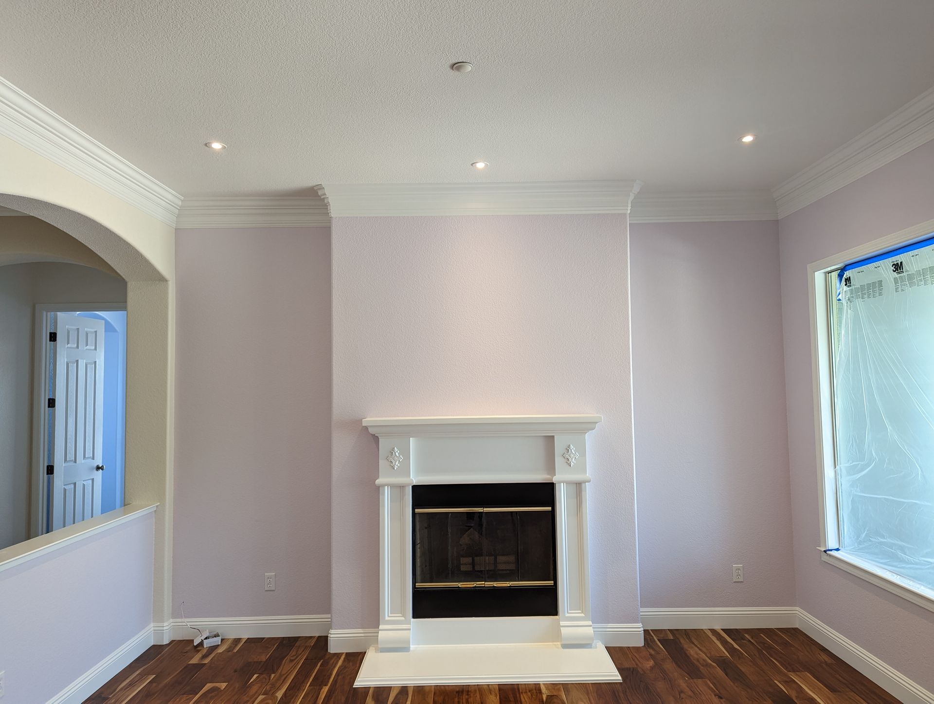 Bright living room with a white fireplace, light lavender walls, arched opening, and window blinds