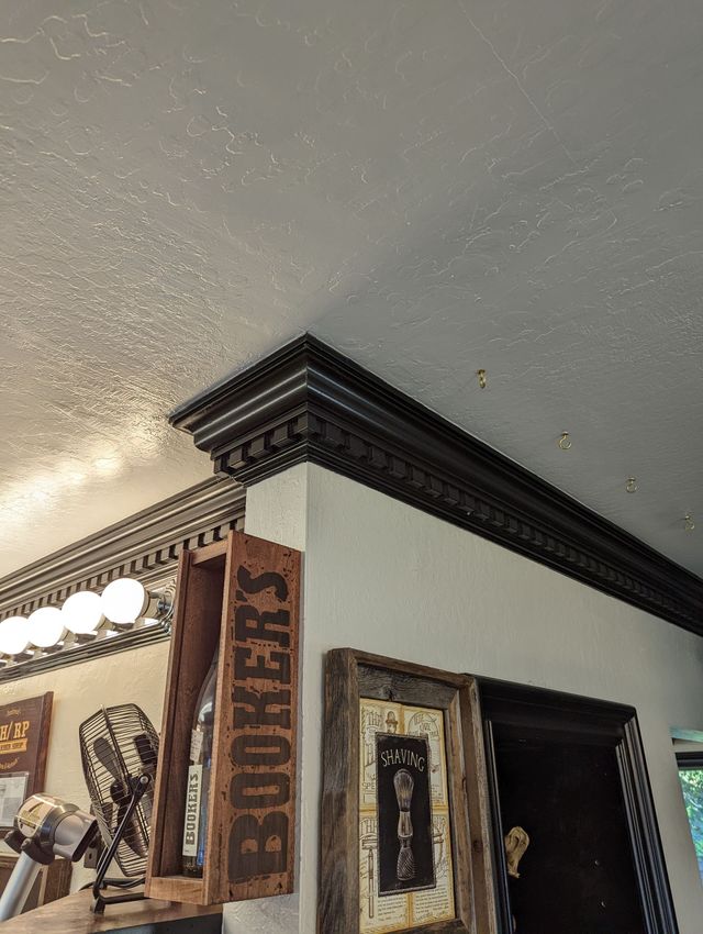 Decorative interior corner with ornate dark wood trim, framed art, and a white textured ceiling