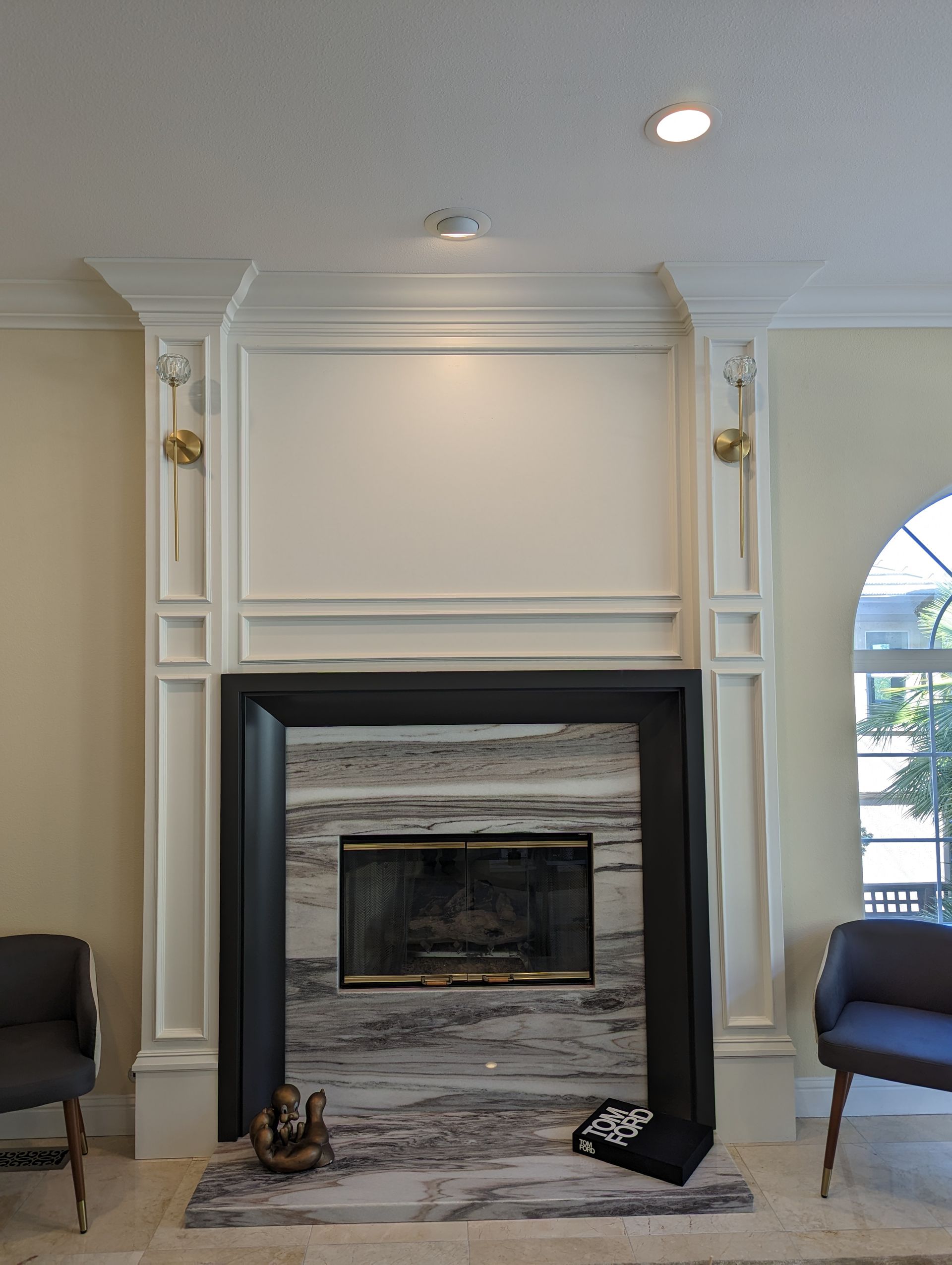 Elegant living room fireplace with white mantel, gray stone surround, and two chairs by an arched window.