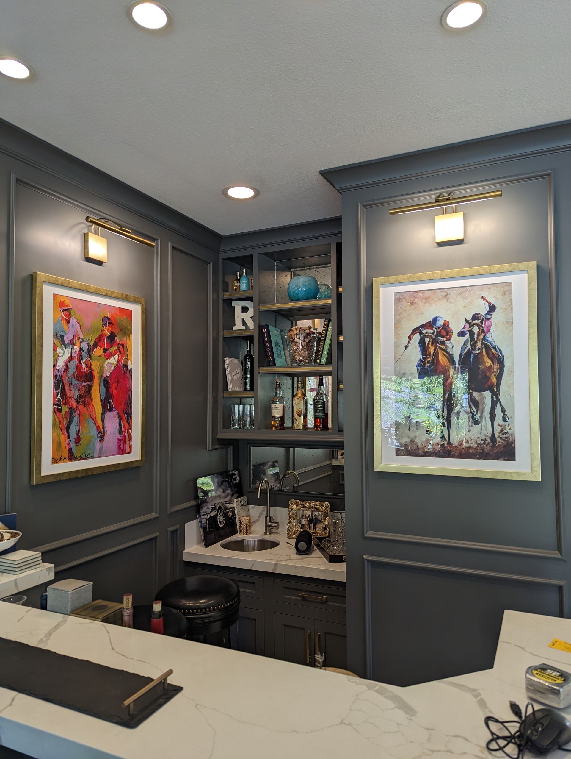 Small home office with gray built-ins, white desk, and colorful framed art under recessed ceiling lights