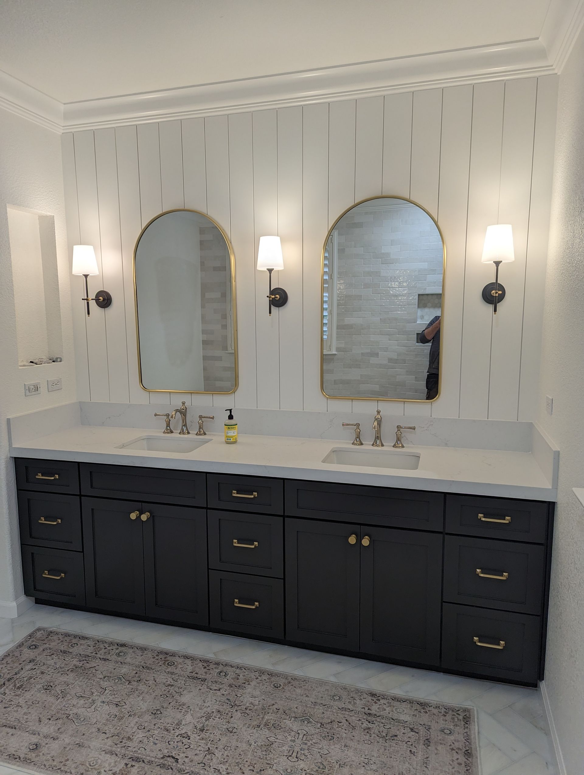 Elegant bathroom vanity with twin arched mirrors, wall sconces, and dark cabinets beneath a white countertop