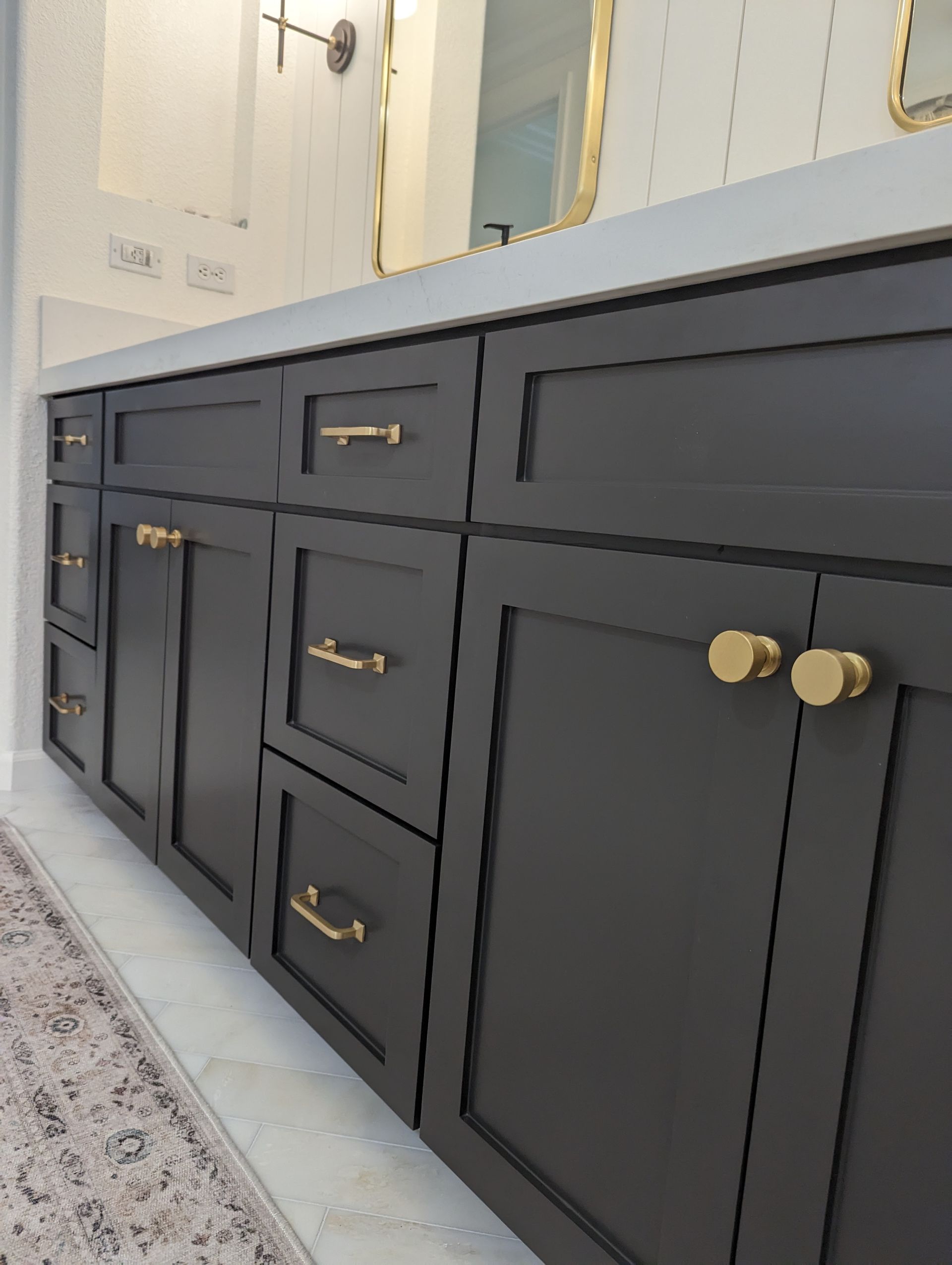 Dark gray bathroom vanity with gold knobs and a white countertop beneath a mirror.