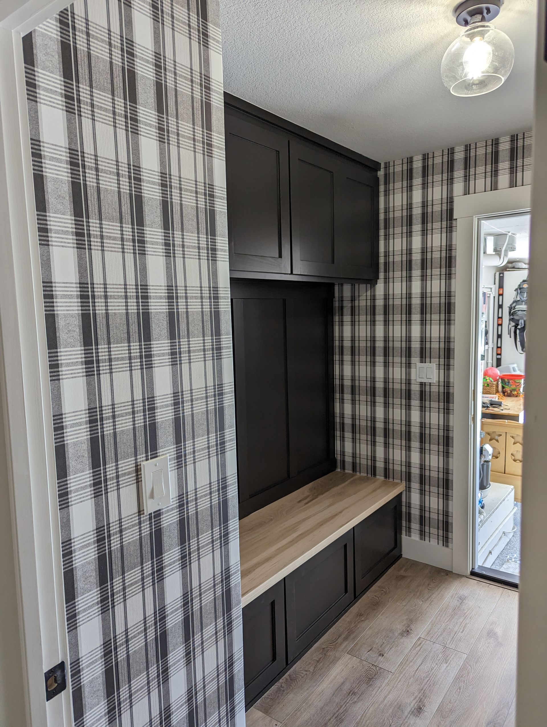 Built-in black cabinet with wood bench in a small room with plaid curtains and mirrored closet doors