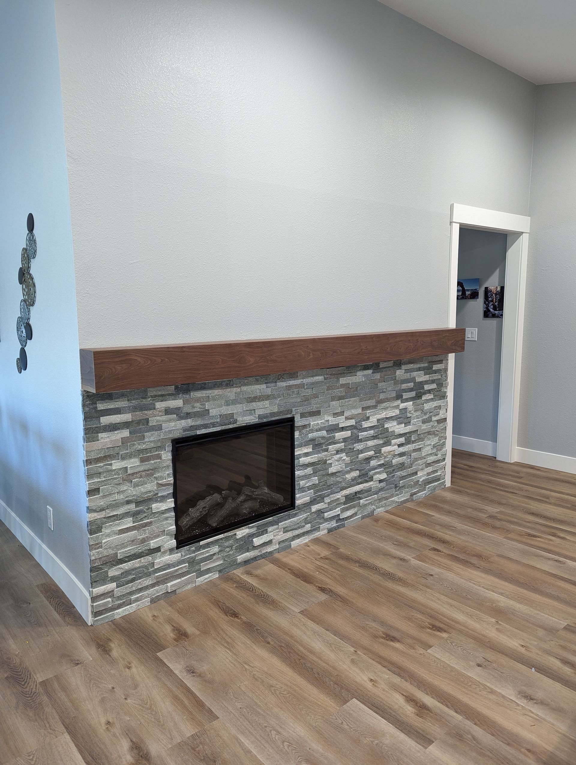 Empty living room with gray stone fireplace, white walls, and wood flooring.