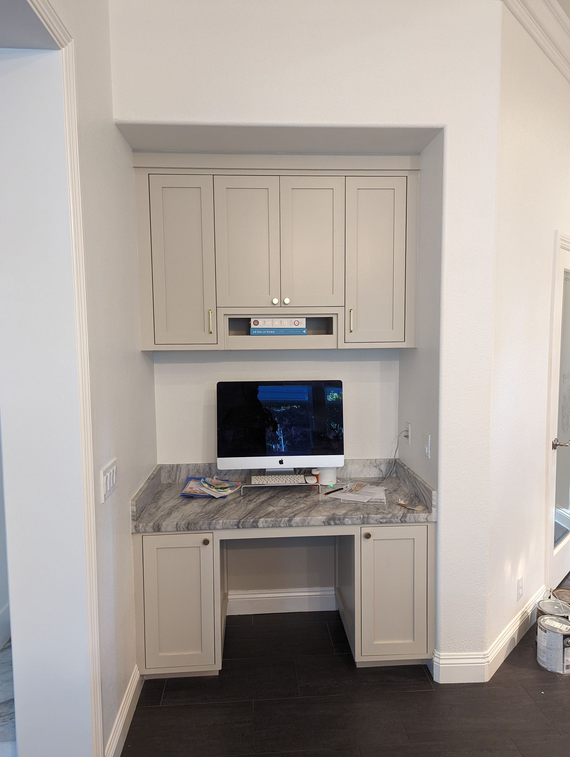 Built-in desk nook with beige cabinets, marble-look countertop, and a computer monitor on a dark floor