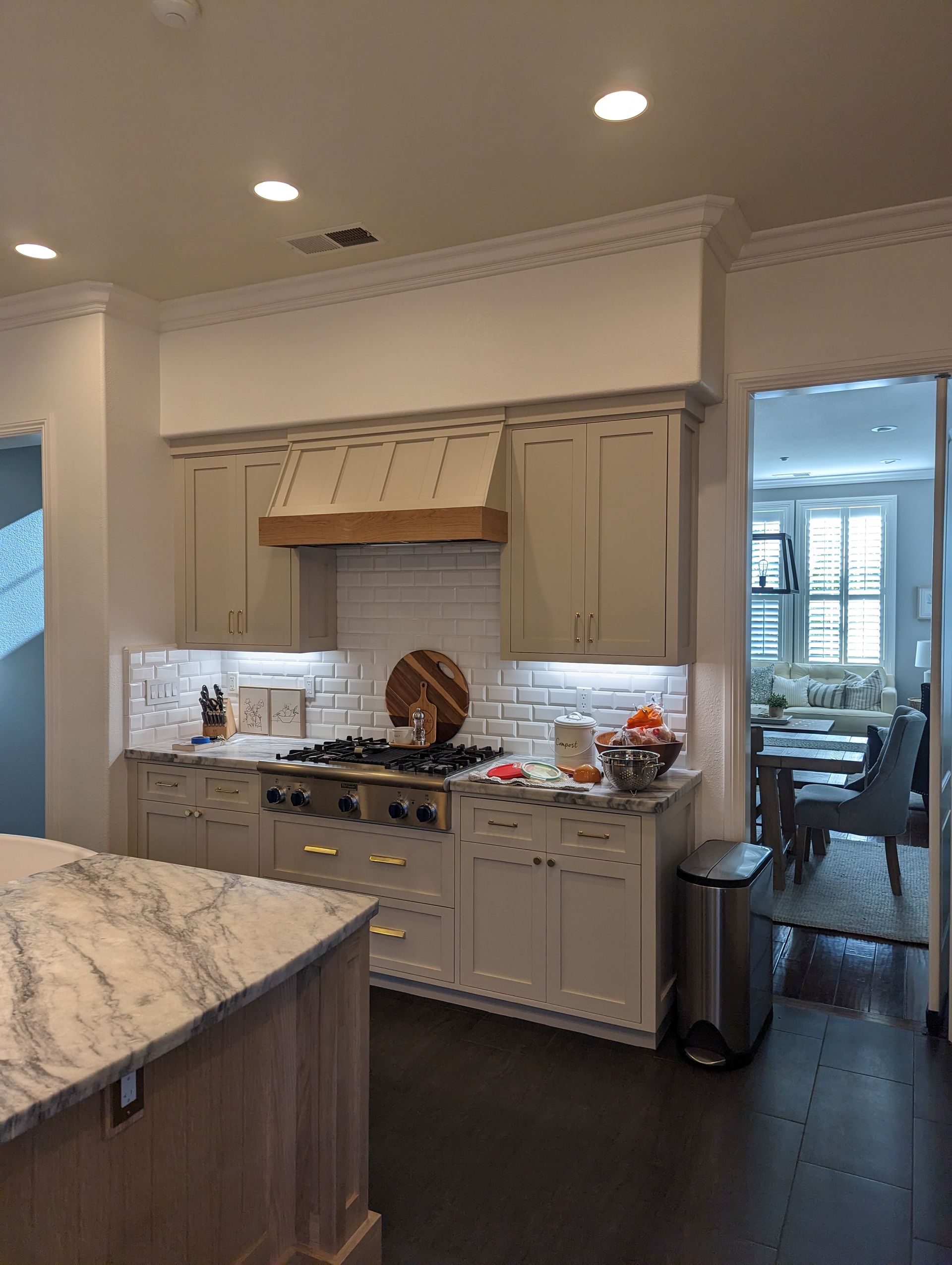 Modern kitchen with white cabinets, marble island, gas range, and dark wood floor, lit by recessed ceiling lights