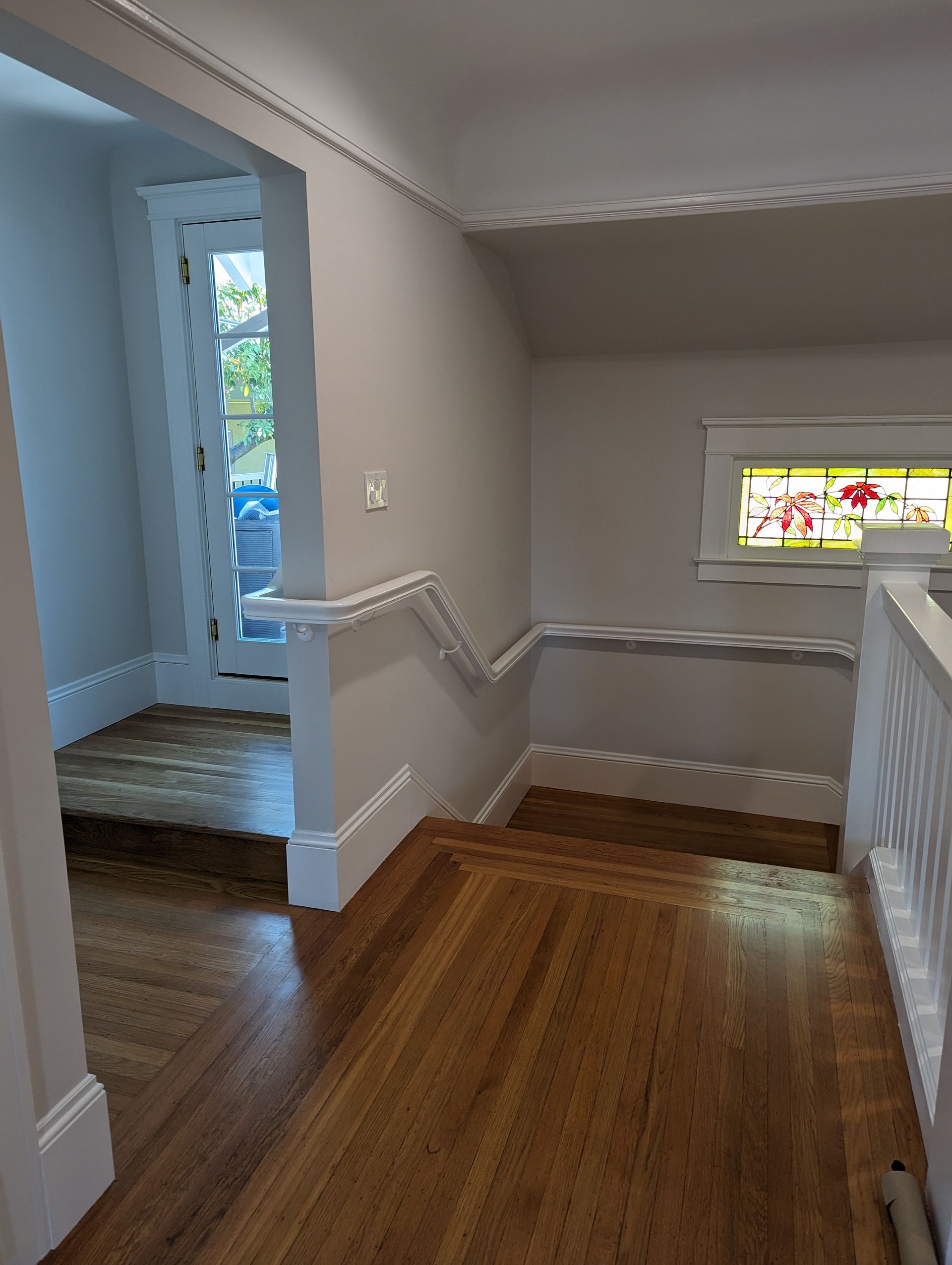 Interior hallway with hardwood floor, beige walls, and a stained-glass window by the stairs.