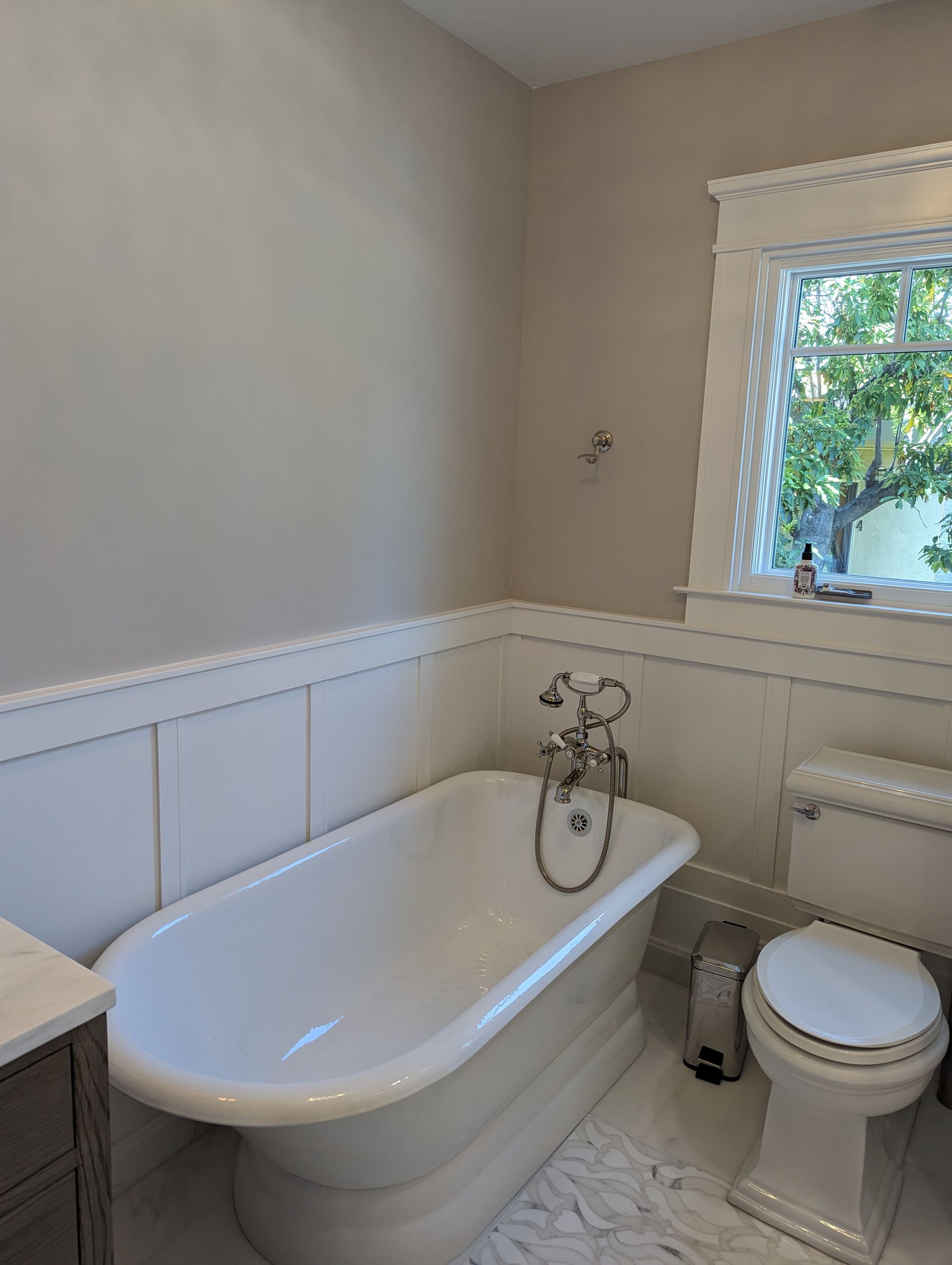 Small bathroom with a white clawfoot tub, toilet, window, and light-colored walls