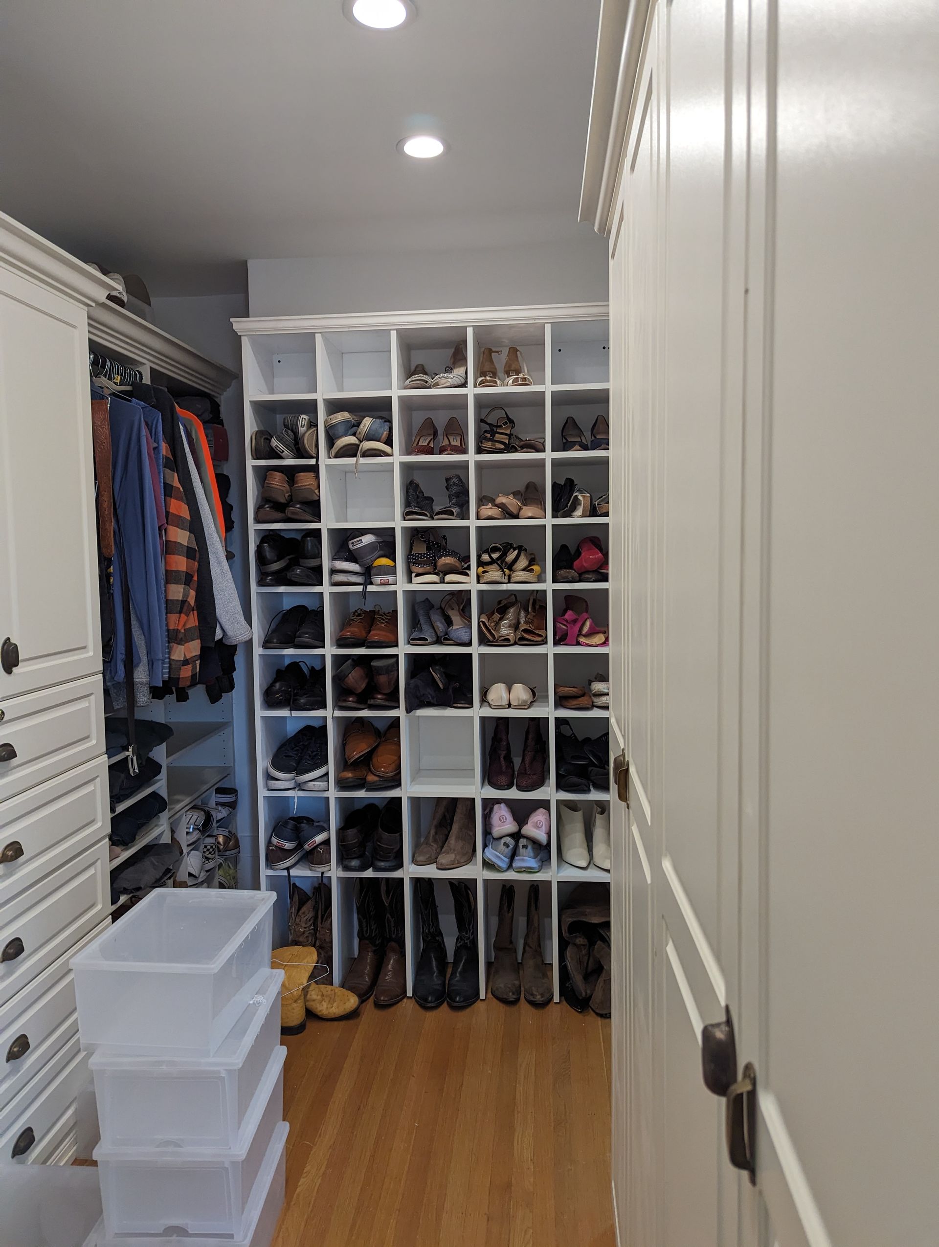 Walk-in closet with white shelving, neatly organized shoes, hanging clothes, and stacked storage bins