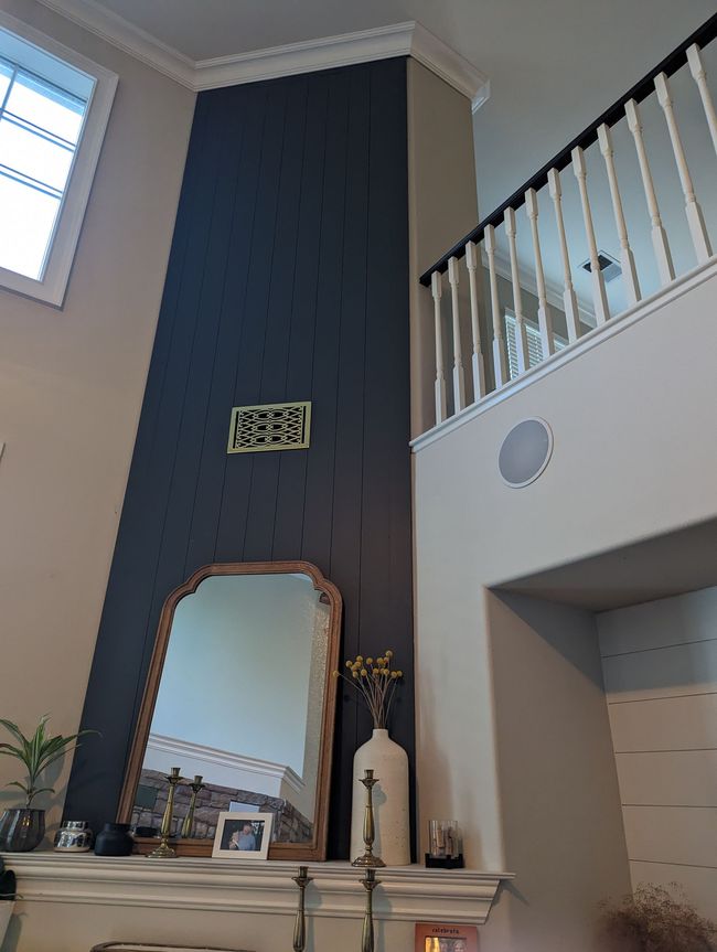 Living room with tall dark accent wall, mirror over fireplace mantel, and white staircase railing