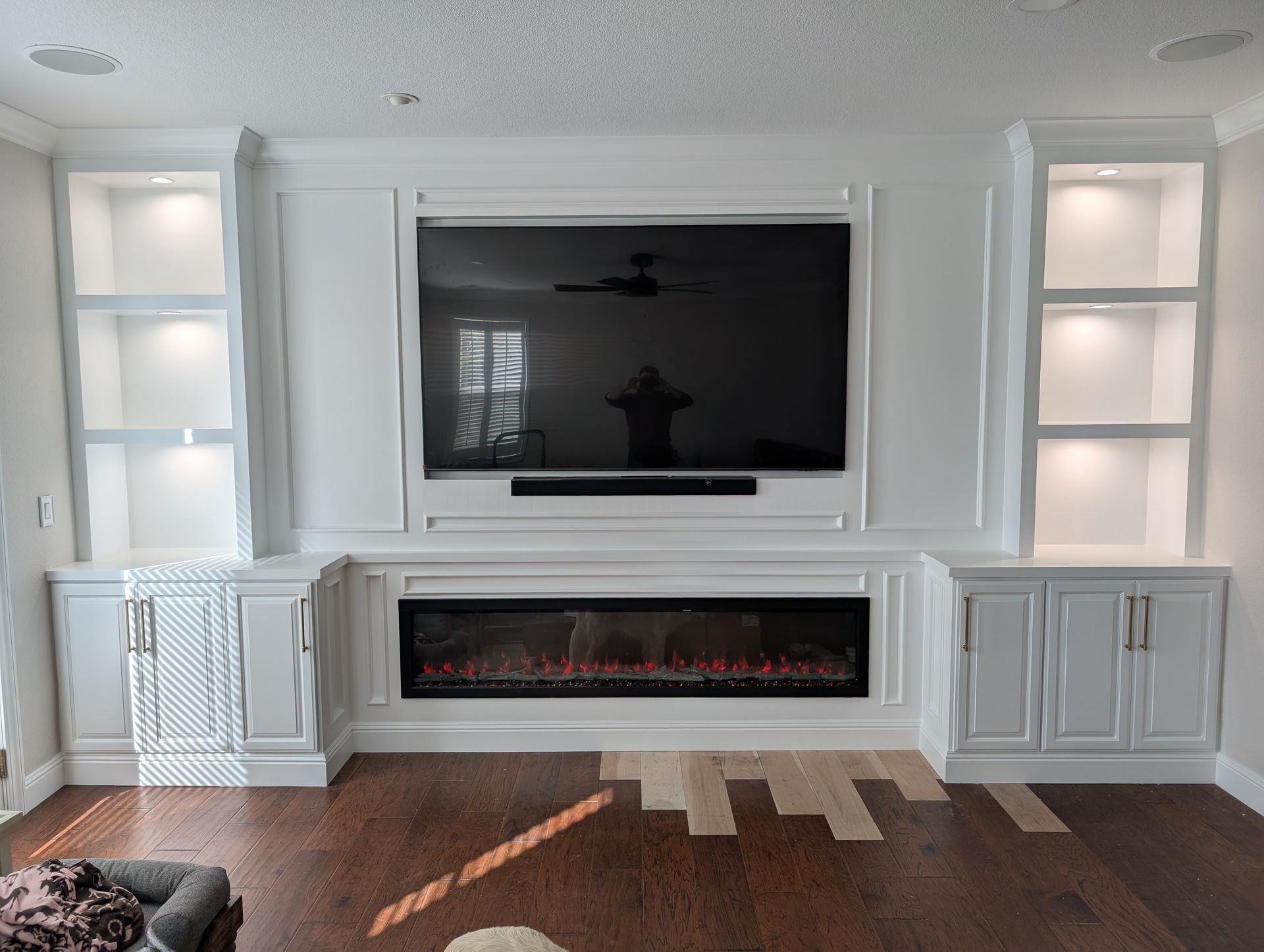 White living room wall with mounted TV above an electric fireplace and built-in lit cabinets.
