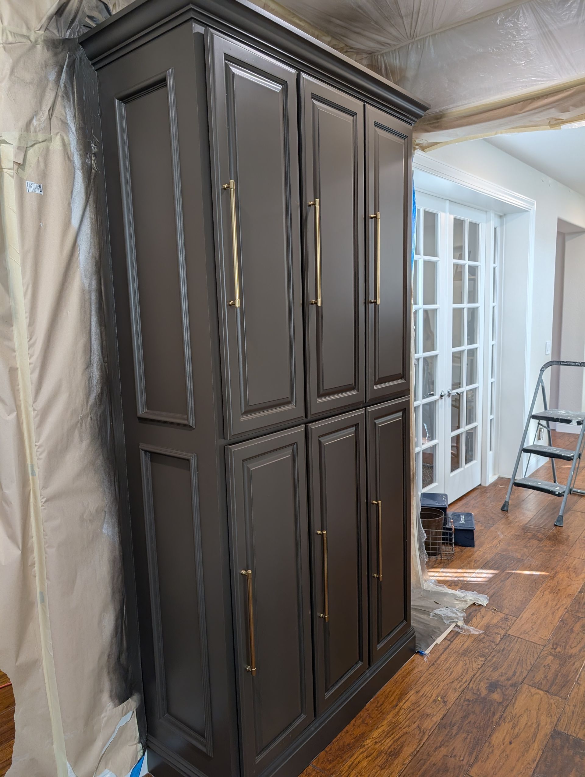 Tall dark armoire in a room with hardwood floors and a doorway to a bright hall