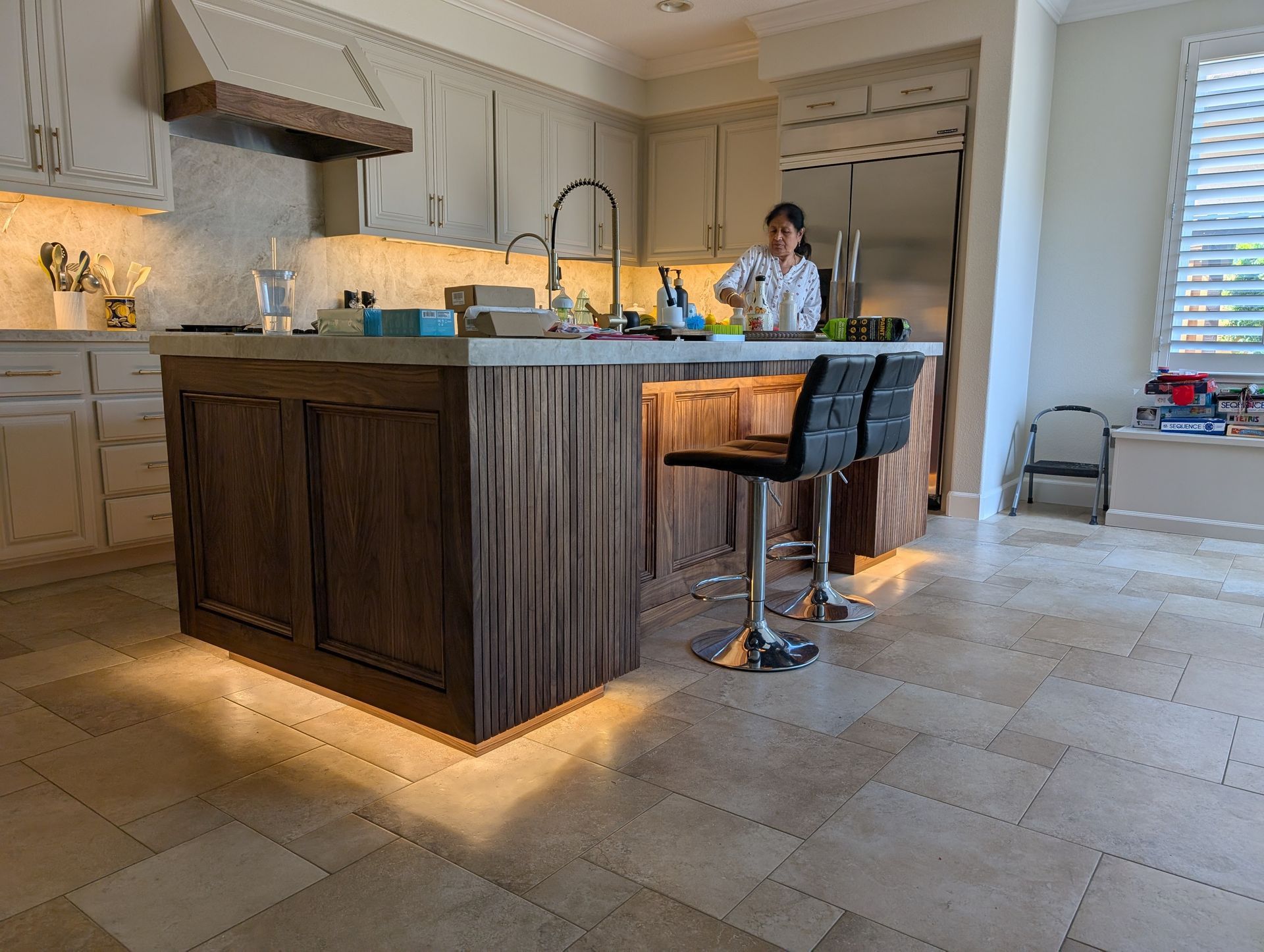 Modern kitchen with a large wood island, lit base cabinets, and a person standing by the sink