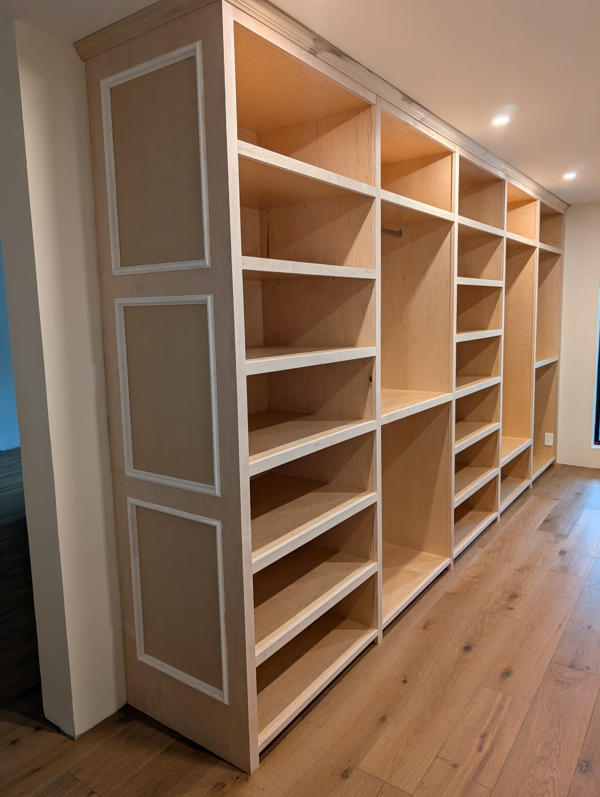 Built-in white shelving unit in a bright hallway with light wood floors.