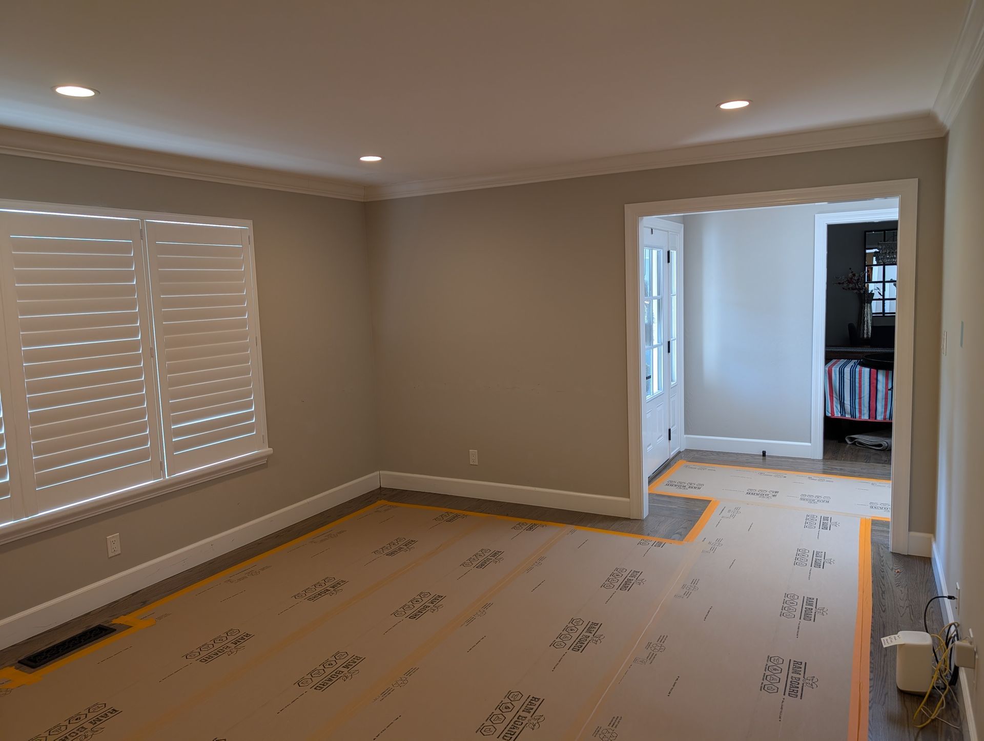 Empty beige living room with recessed lights, window shutters, and carpet being installed