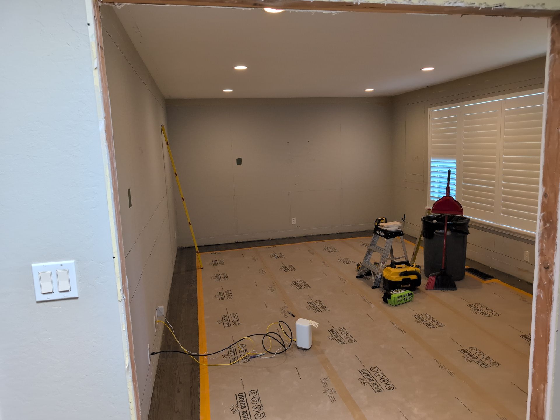 Partially empty room under renovation with protective floor paper, tools, and blinds by the window