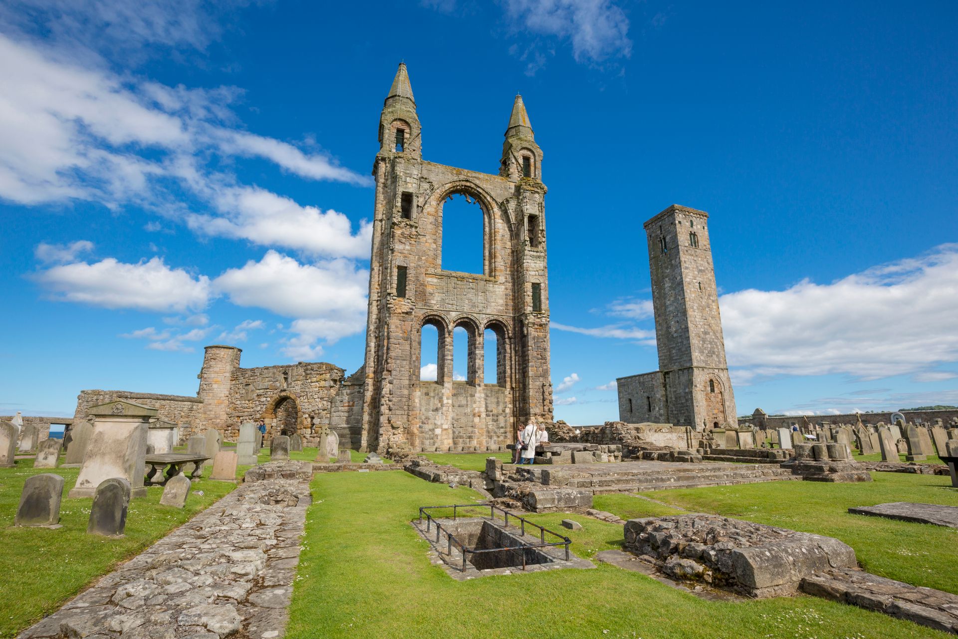 Ruined stone cathedral against a blue sky, graveyard in front.
